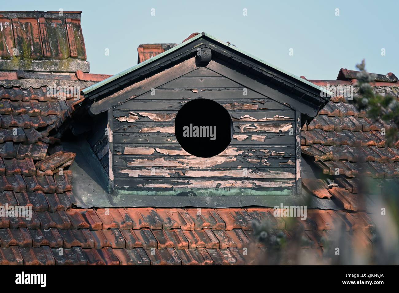 An old house roof with chipped paint and a round window with the sunlight shining on it Stock Photo