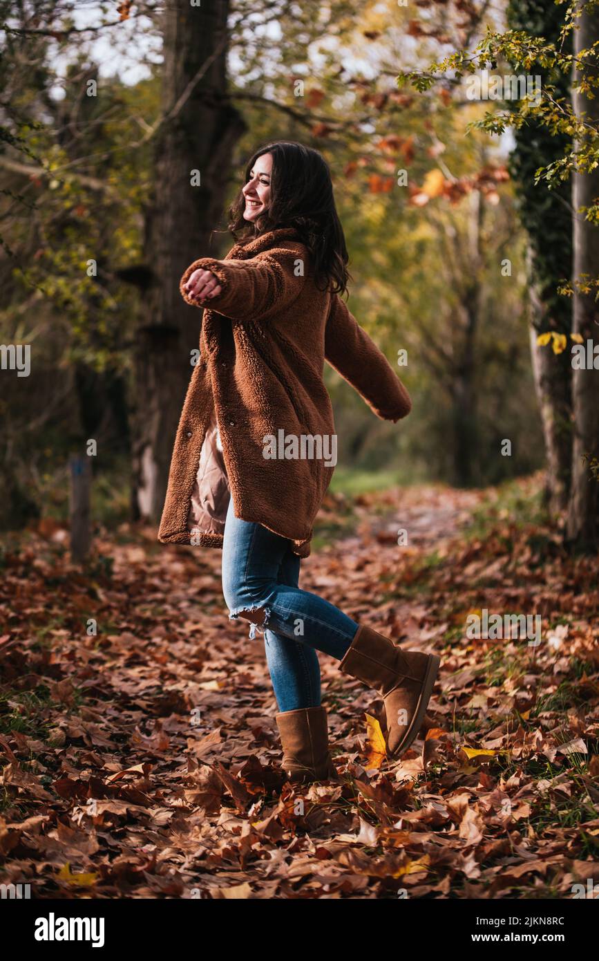 Woman dancing happily on a path covered with dry leaves in autumn. Stock Photo