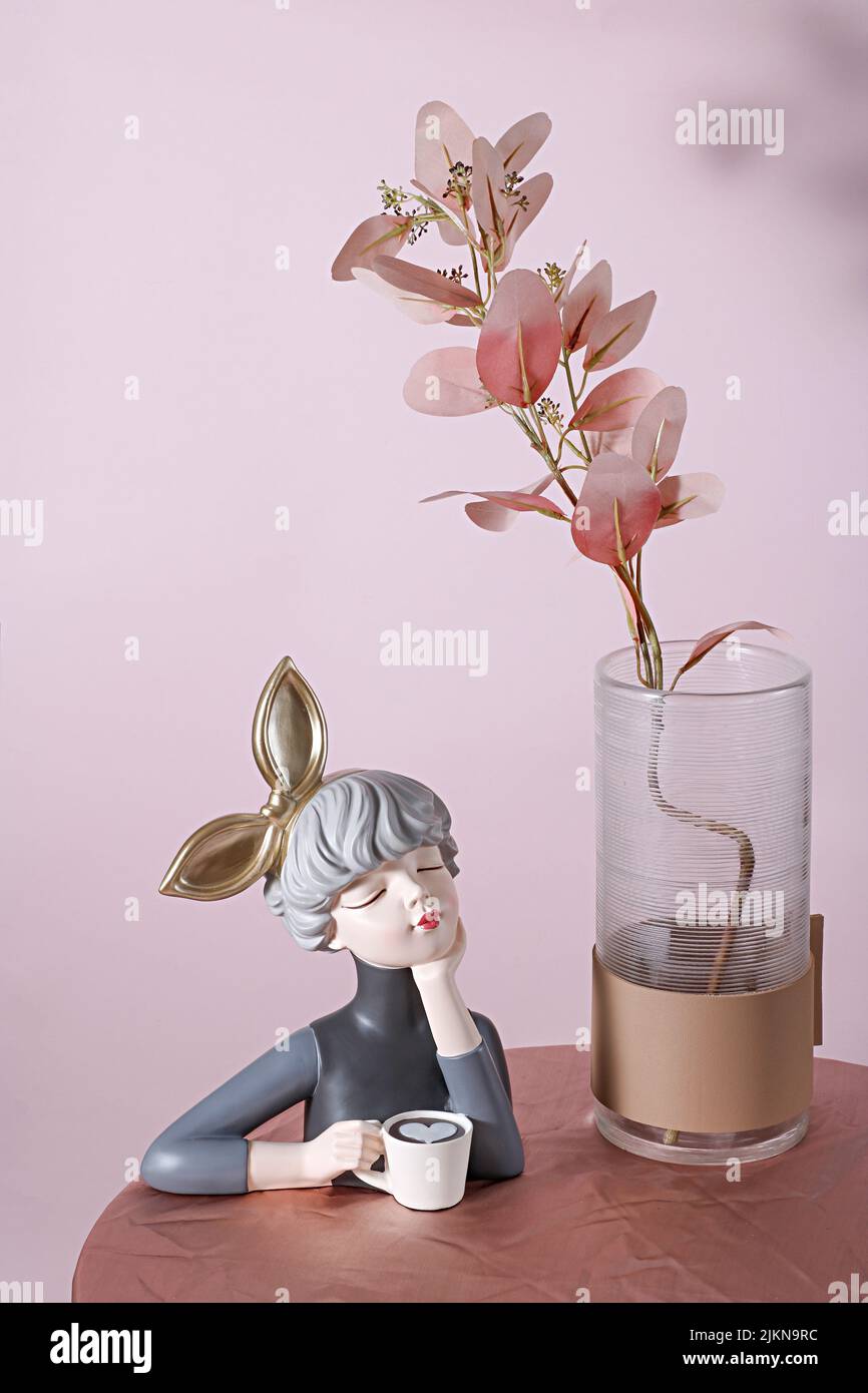 The vertical shot of a fragile porcelain sculpture depicting a girl with a huge golden bow holding a cup of coffee Stock Photo