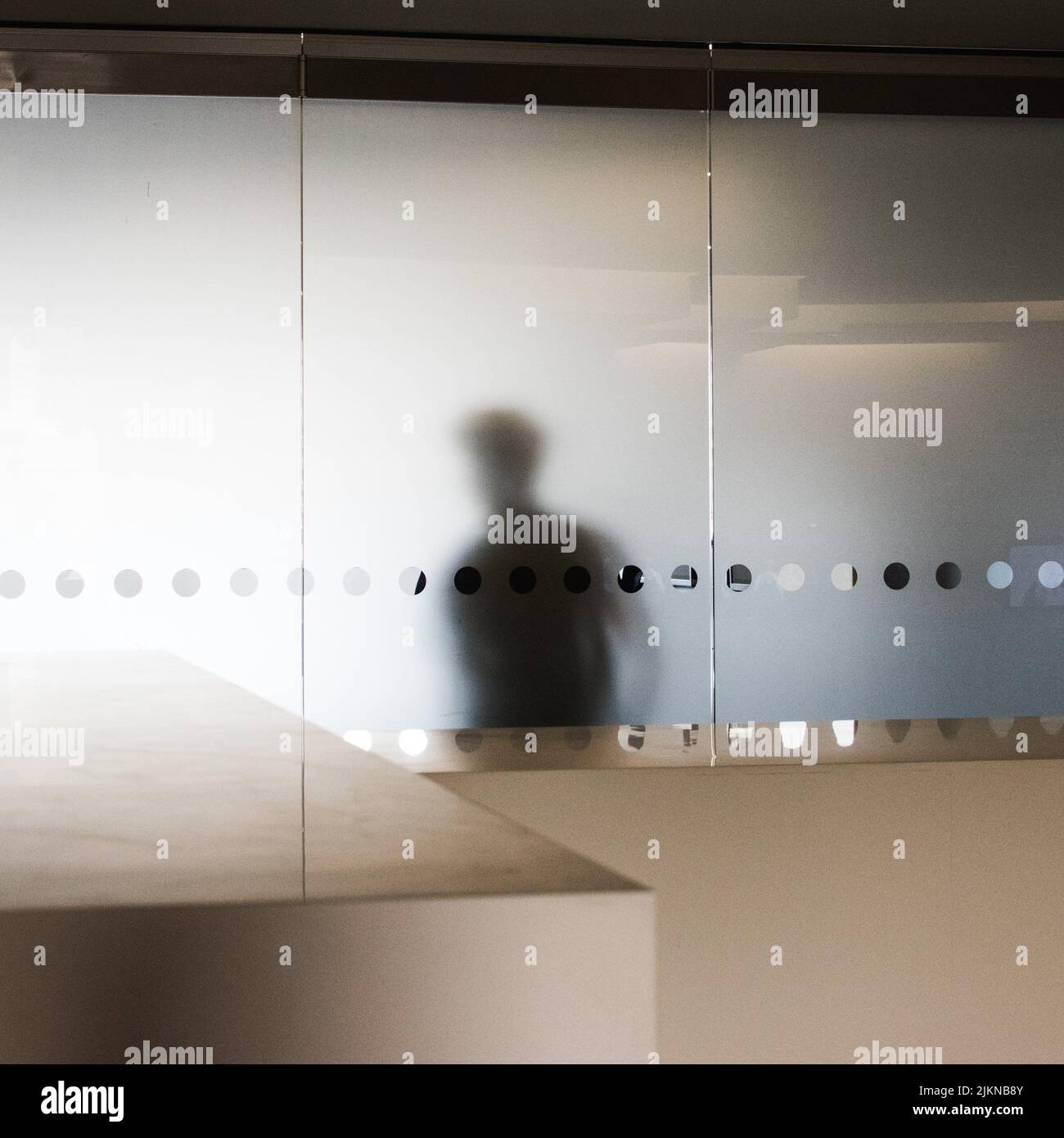 A shot of a man's shadow on a wall from inside glass room Stock Photo