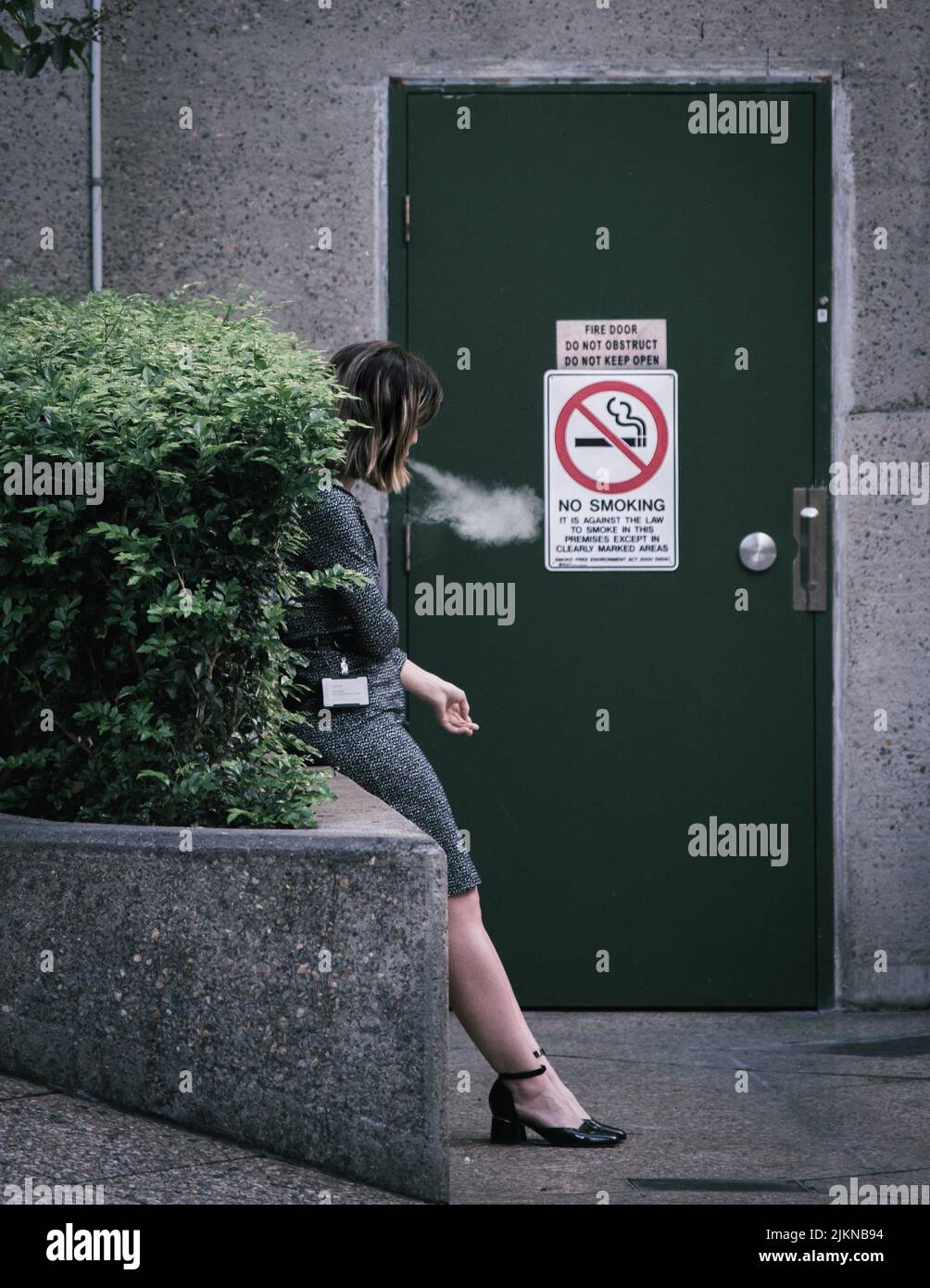 A shot of a woman standing by the plants outside and smoking next to a
