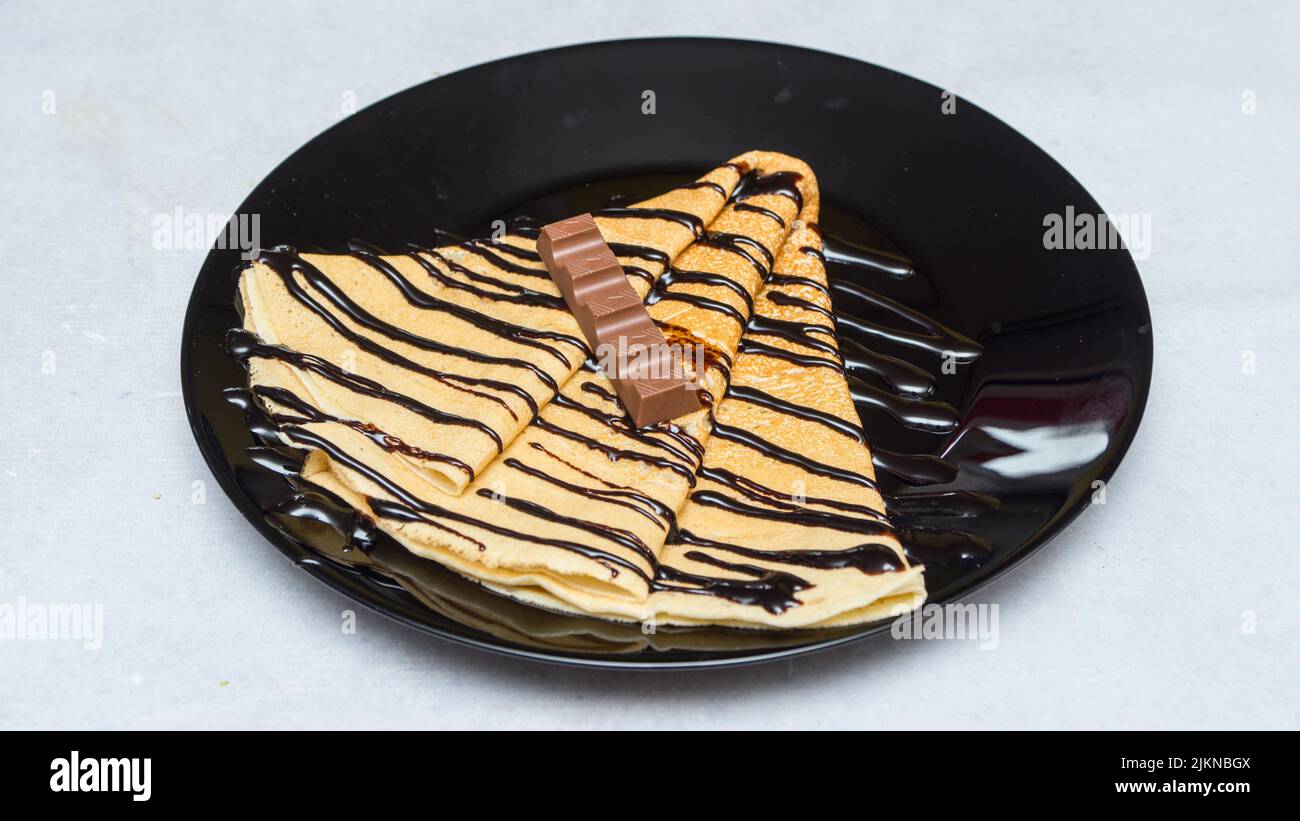 A closeup shot of crepes with chocolate syrup and candy on a black plate Stock Photo