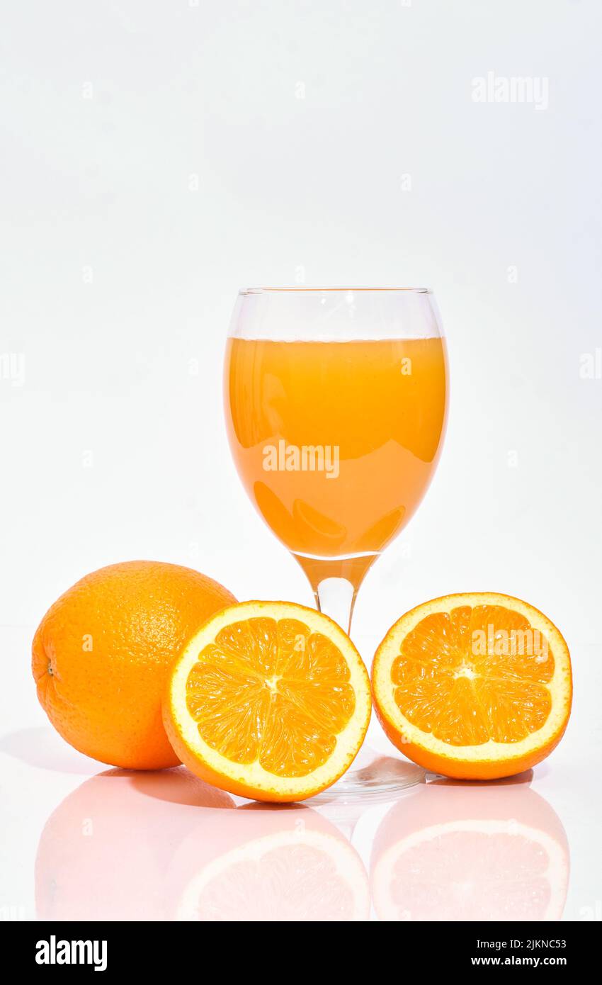 Whole and sliced oranges with a glass of squeezed juice on white