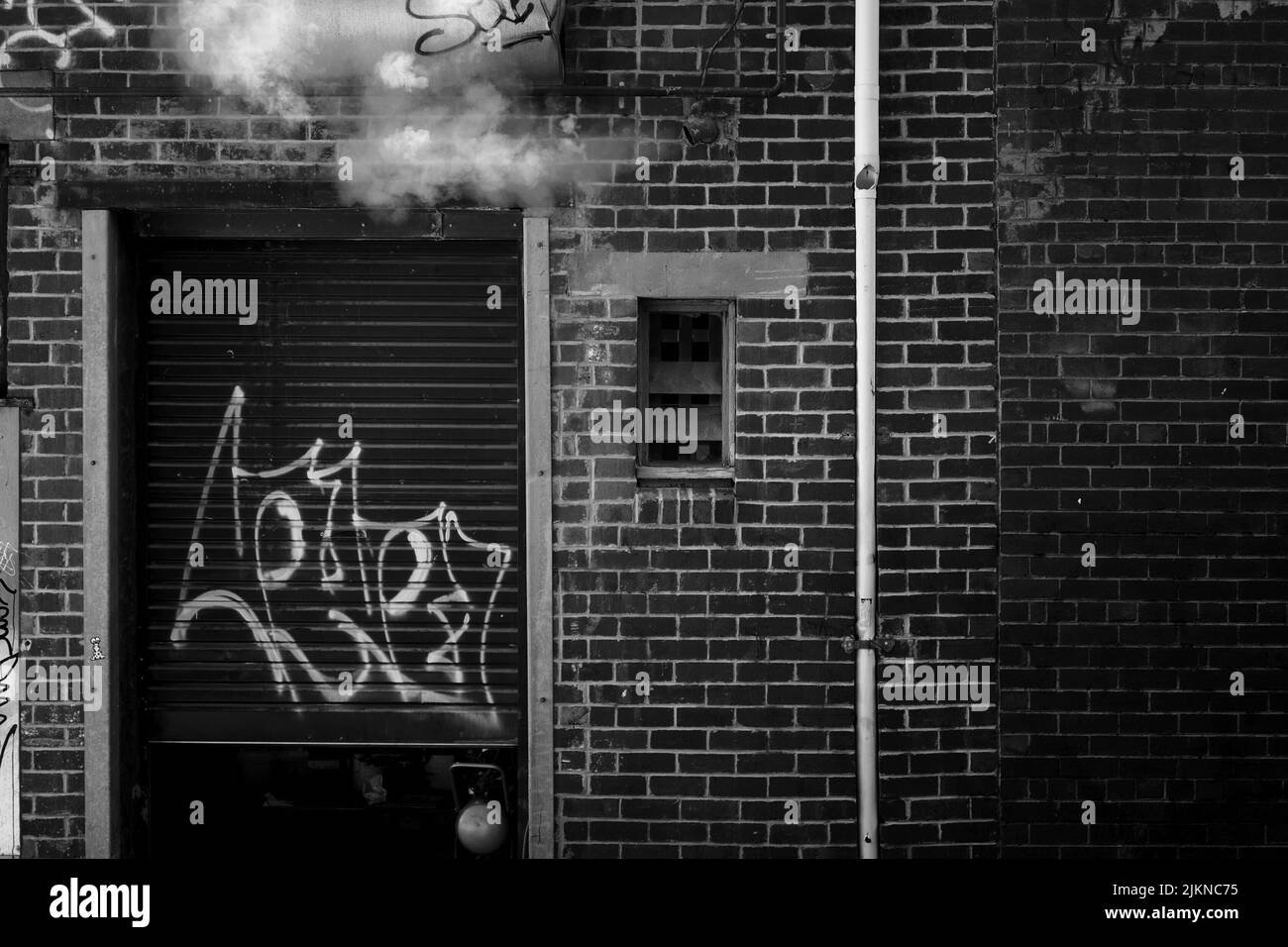A grayscale shot of graffiti on the rear entrance of a dry cleaner, back alley. Melbourne. Australia. Stock Photo
