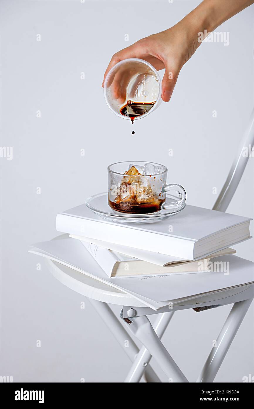 A vertical shot of a hand gradually adding coffee to a cup with ice cubes on a white background Stock Photo