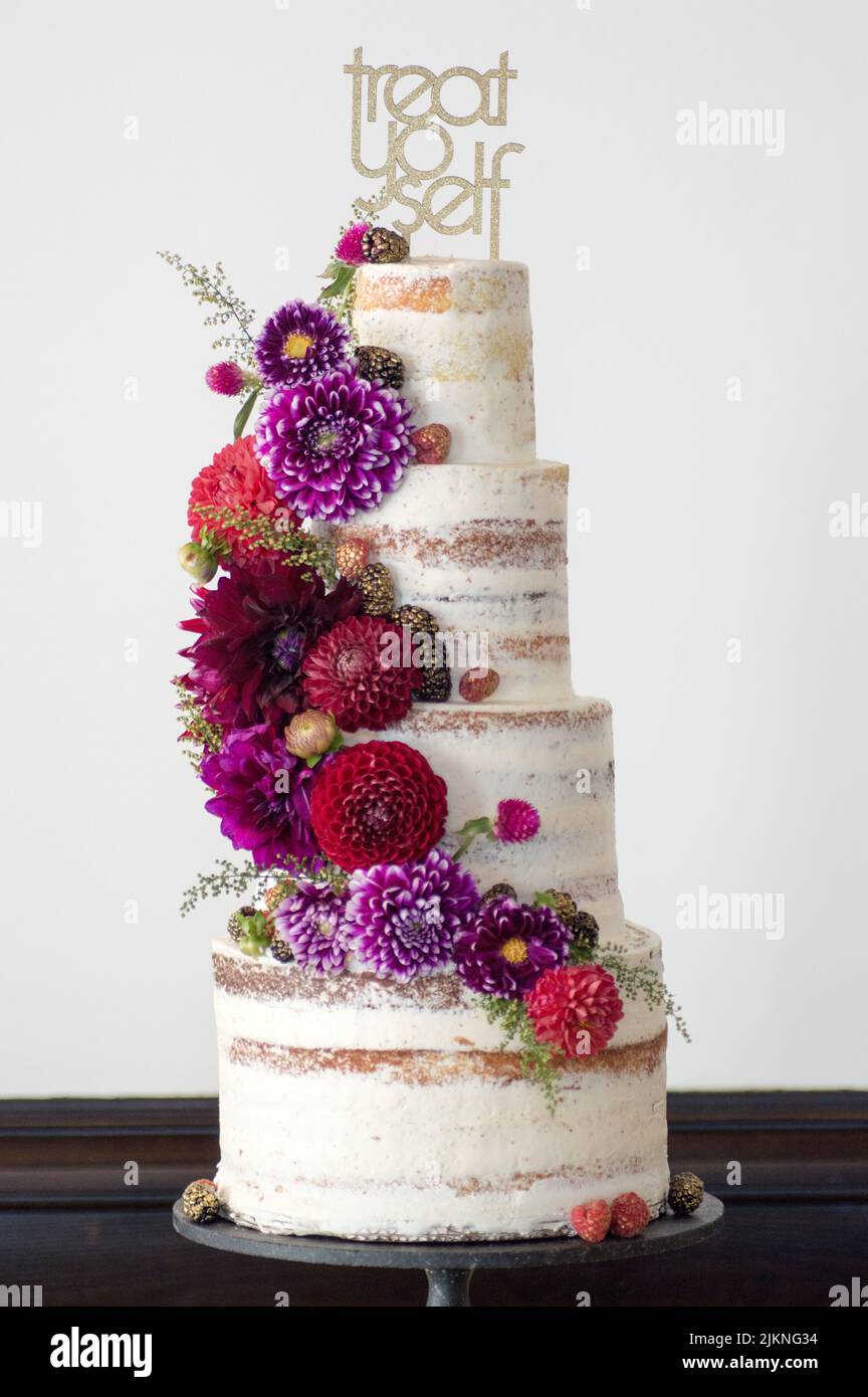 A vertical shot of a large 4 tier cake with colorful fresh flowers on a white background Stock Photo