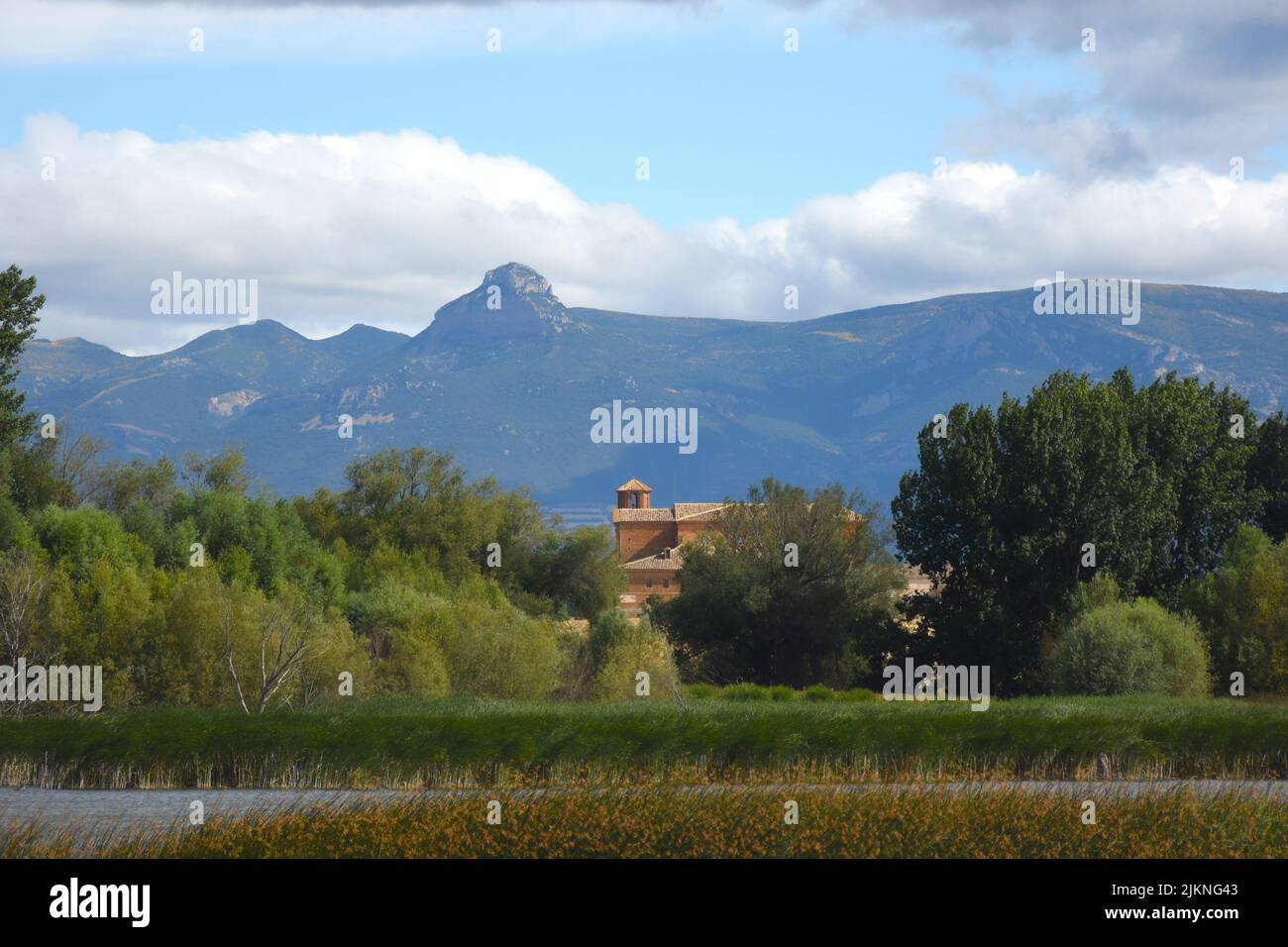 A landscape view of trees and a small brown building in the background of mountains and a cloudy sky Stock Photo
