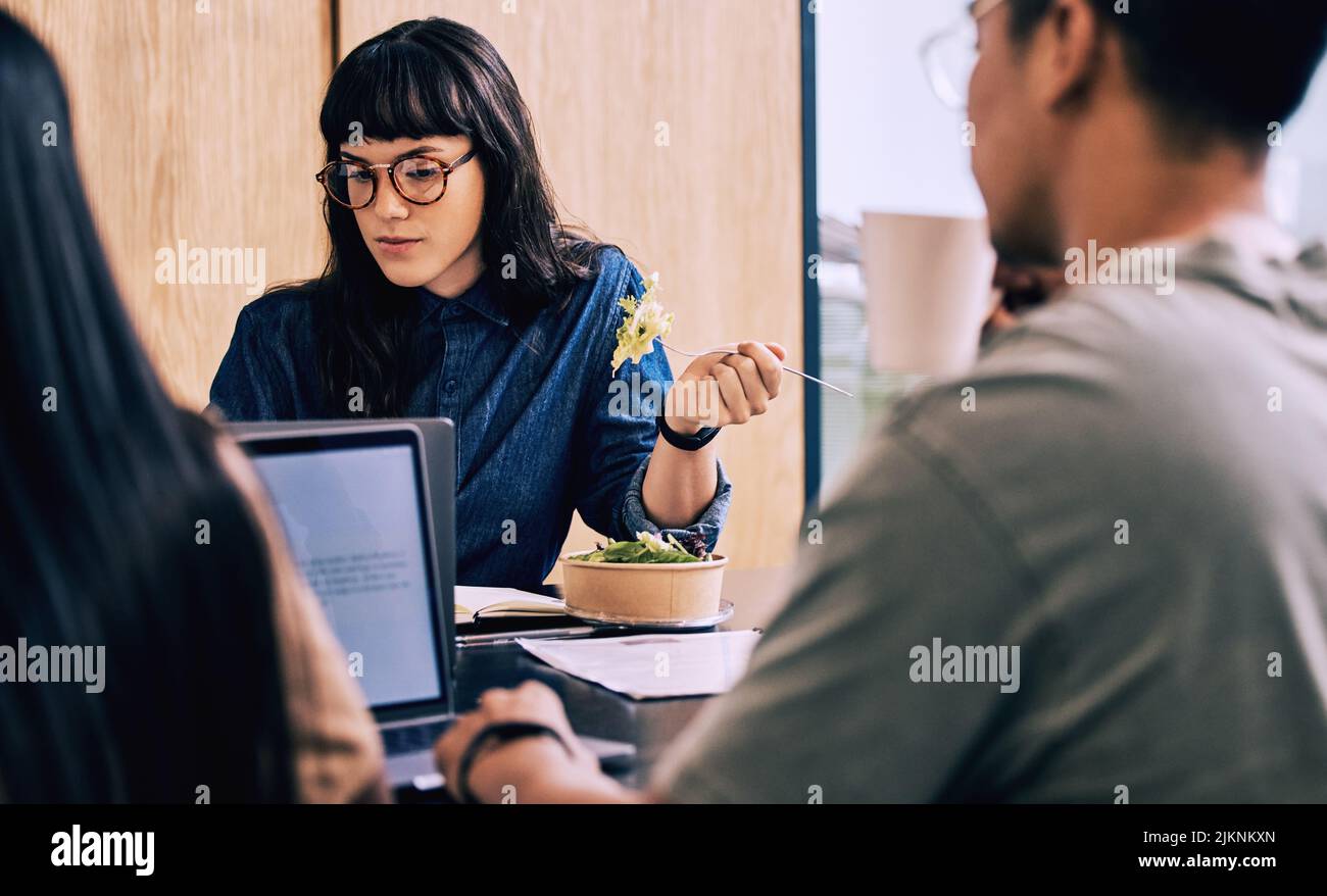 This salad is to tasty. a young businesswoman eating while with her coworkers. Stock Photo