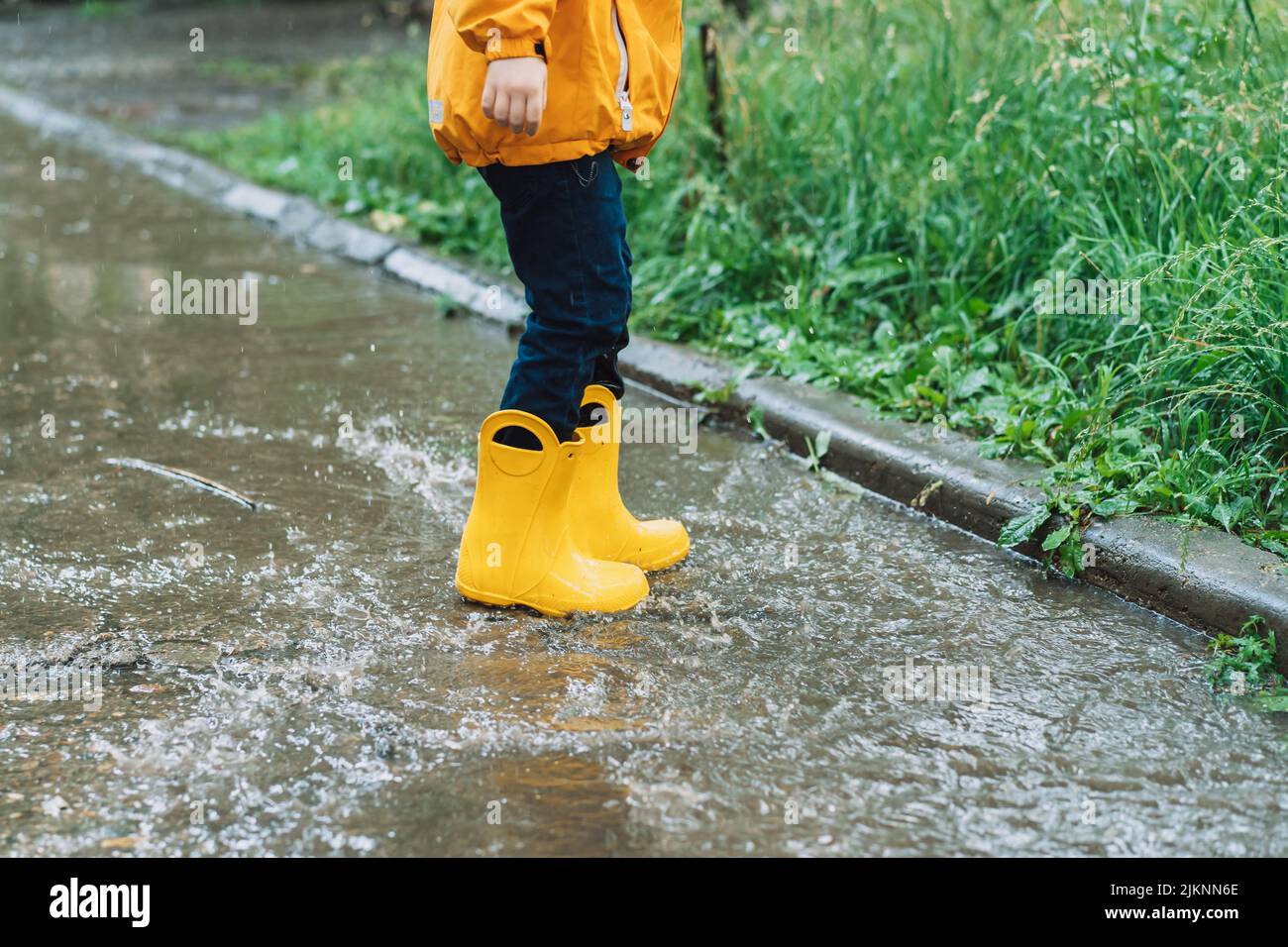 Child in yellow rubber boots jumping through puddles Stock Photo Alamy