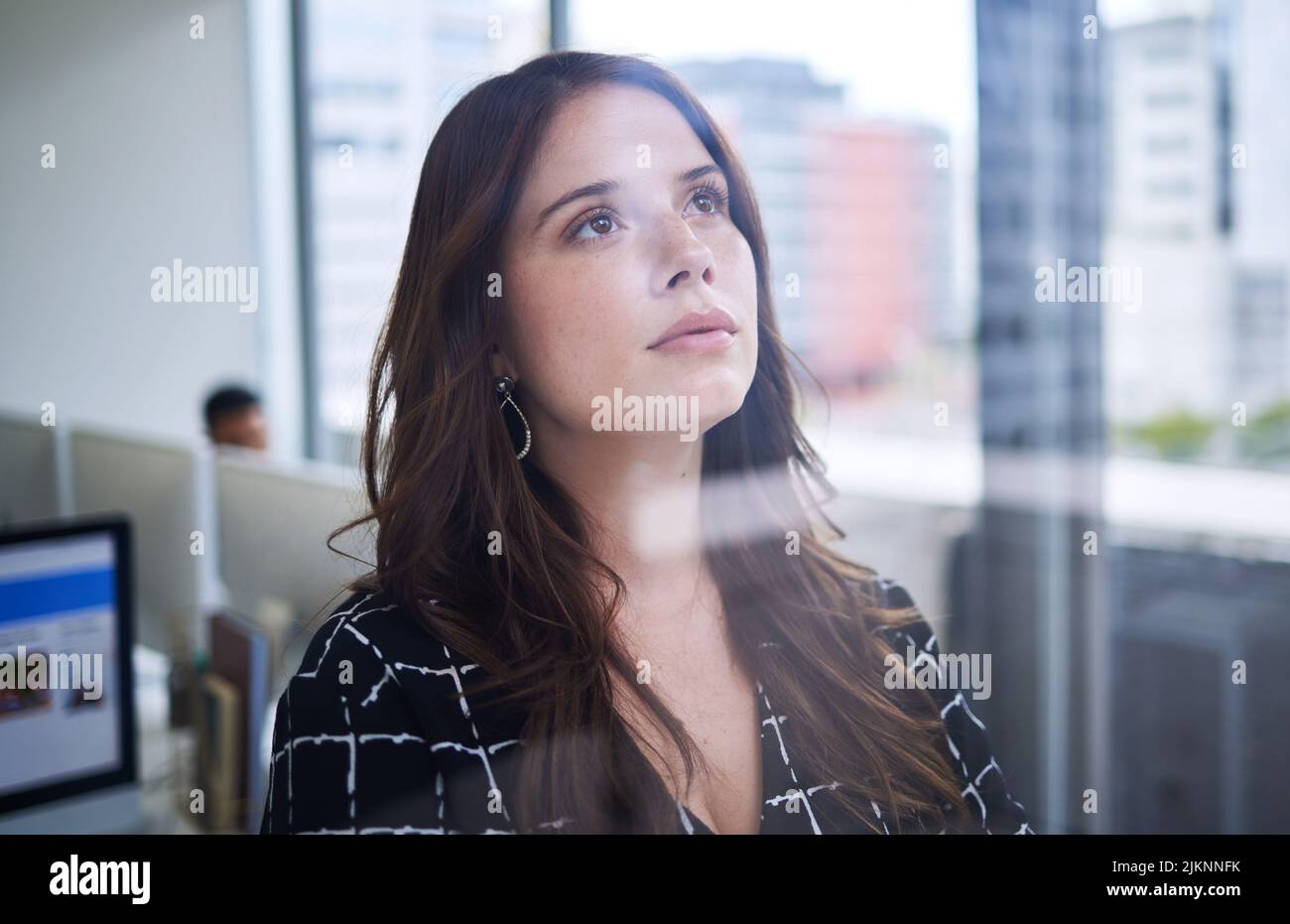 Have the courage to pursue your dreams. a young businesswoman looking thoughtful while standing at a window in an office. Stock Photo