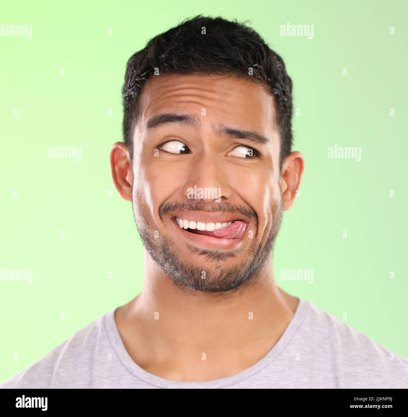 Hes a little unsure. a handsome young man making a face against a green background in studio. Stock Photo