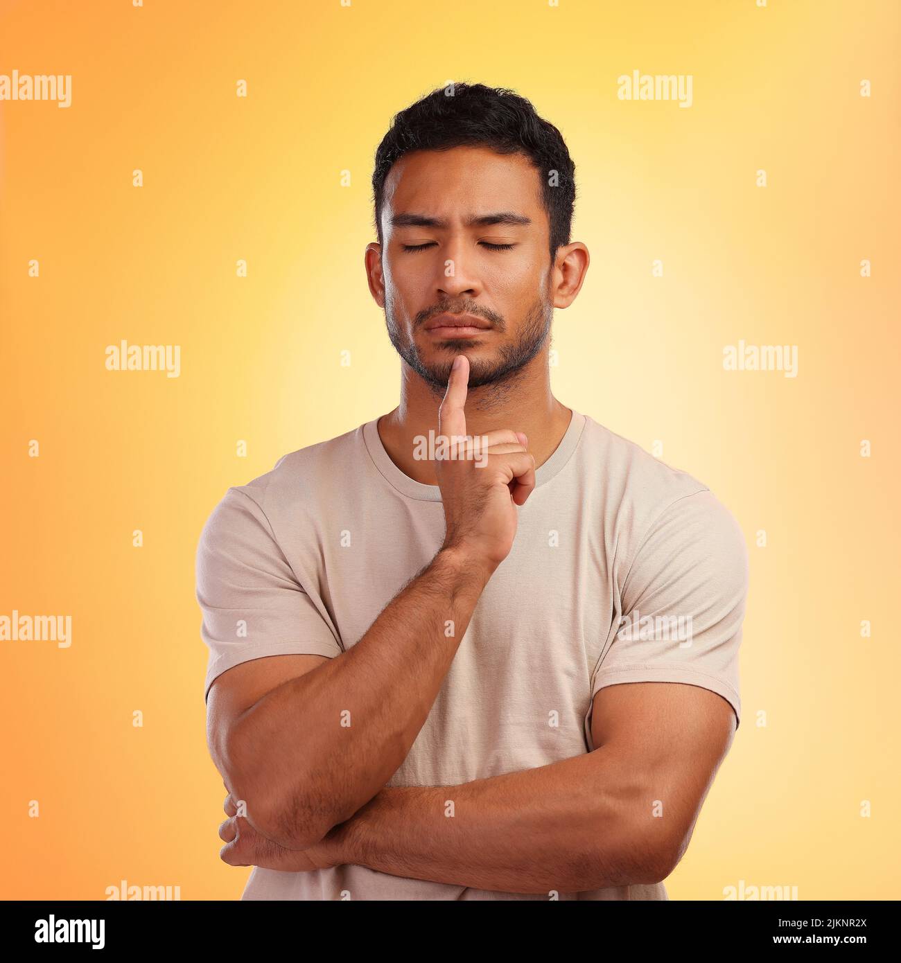 I need some time to think about it. a young man looking thoughtful while standing against a yellow background. Stock Photo