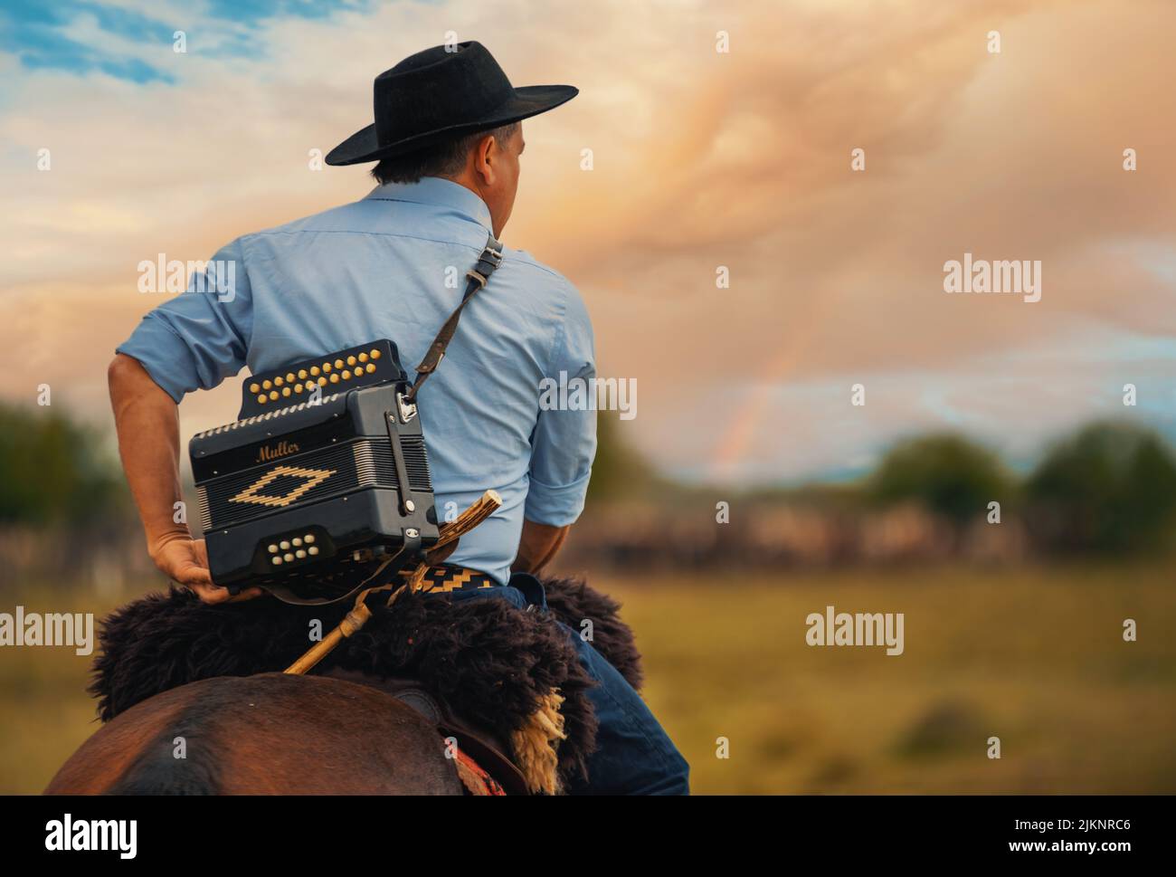 A gaucho riding a horse with an accordion in his back at countryside. Stock Photo