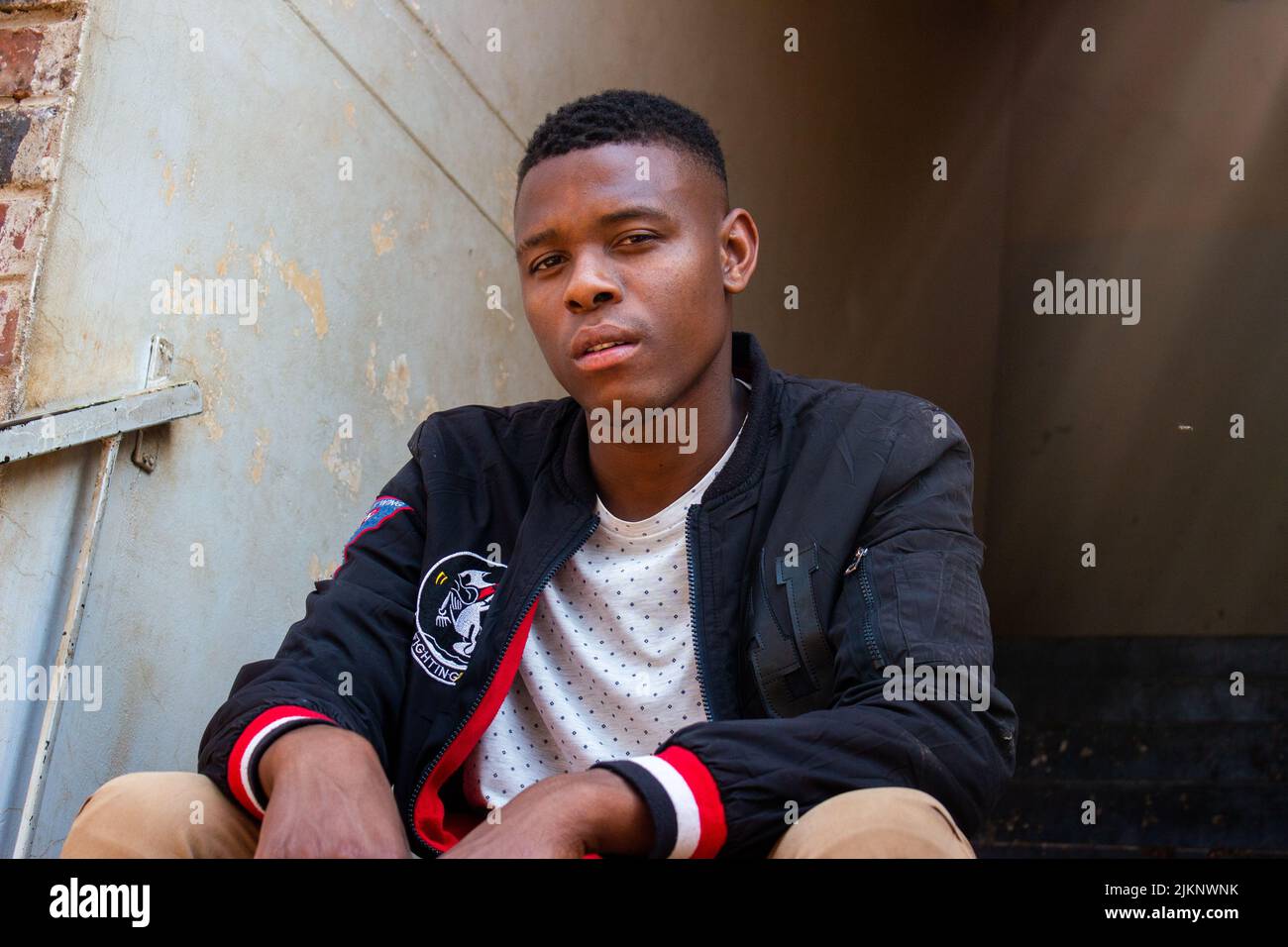 A black man in casual clothes sitting on the stairs and looking at ...