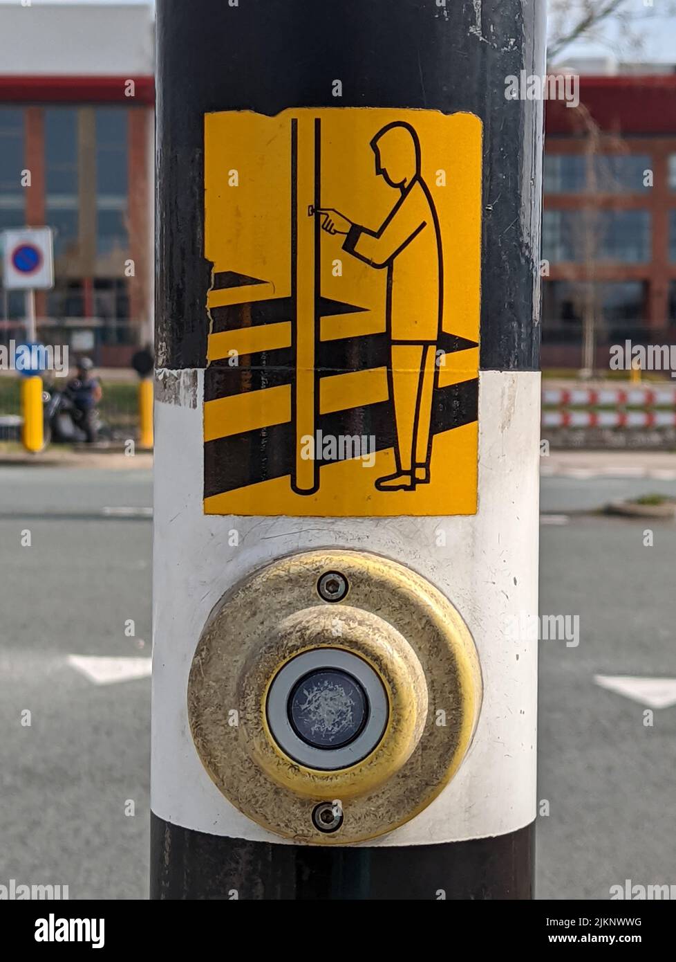 A vertical shot of a pedestrian pushbutton on a pole with a yellow person icon Stock Photo