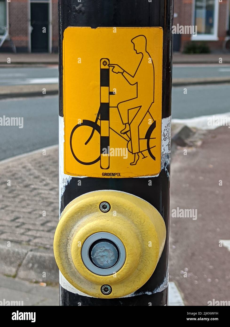 A vertical shot of a bicycle pushbutton on a pole with a yellow cyclist icon Stock Photo