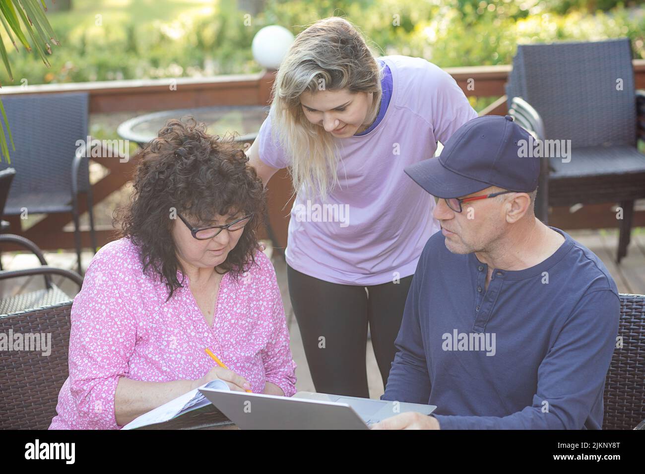 Portrait of family sitting at table. Young woman daughter looking at screen of laptop, explaining to middle-aged couple. Stock Photo
