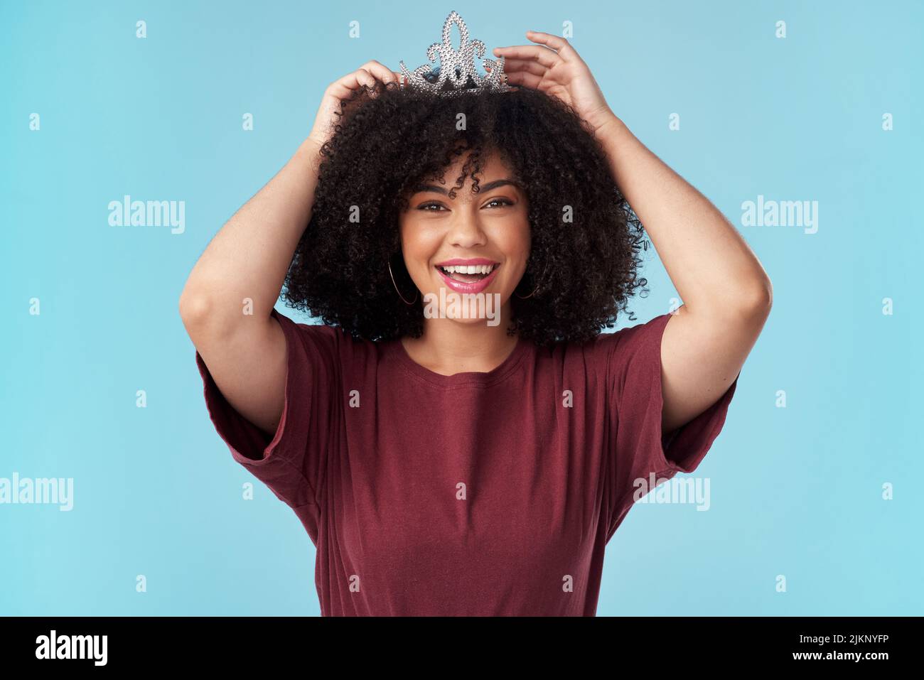 Whats a queen without her king Even more powerful. Studio shot of a young woman putting a crown her head against a blue background. Stock Photo