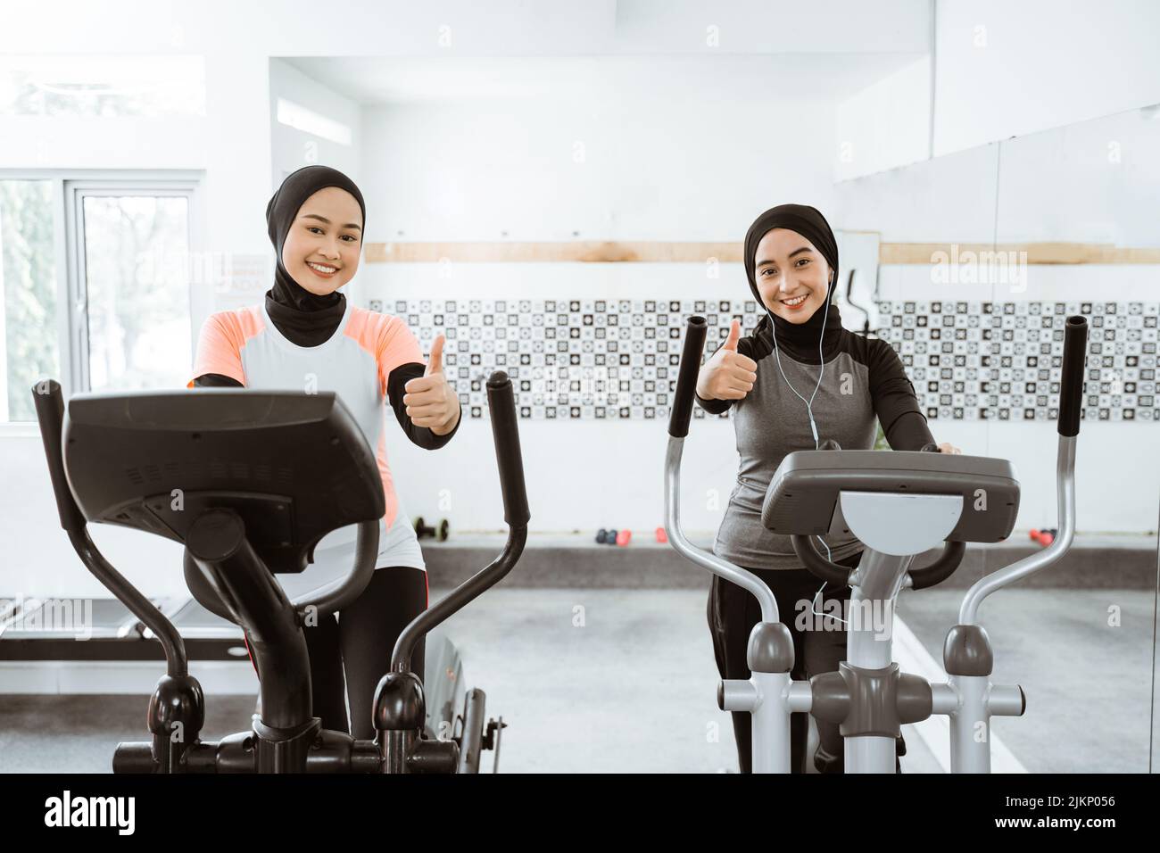 woman exercising with friend on static elliptical cycle machine thumb