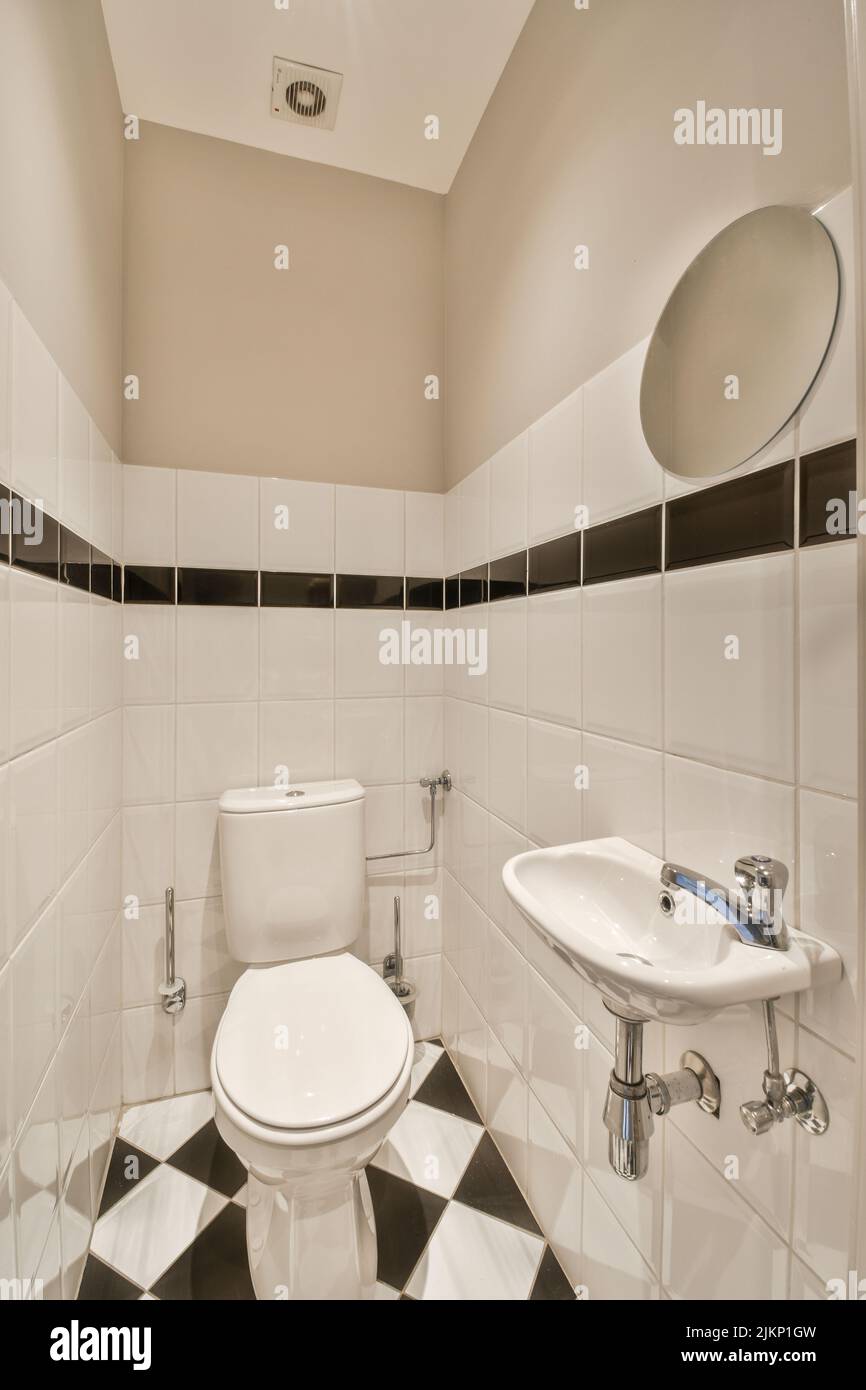 Interior of narrow restroom with sink and wall hung toilet with white
