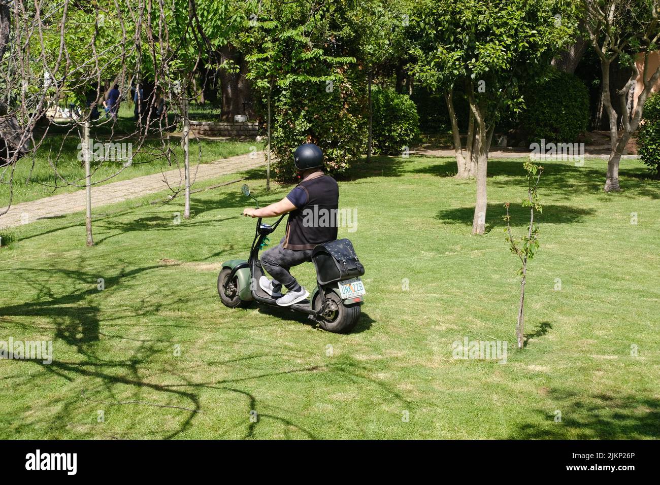 A young man driving a City Coco brand electric scooter on the grass in Fenerbahce Park, Istanbul Stock Photo
