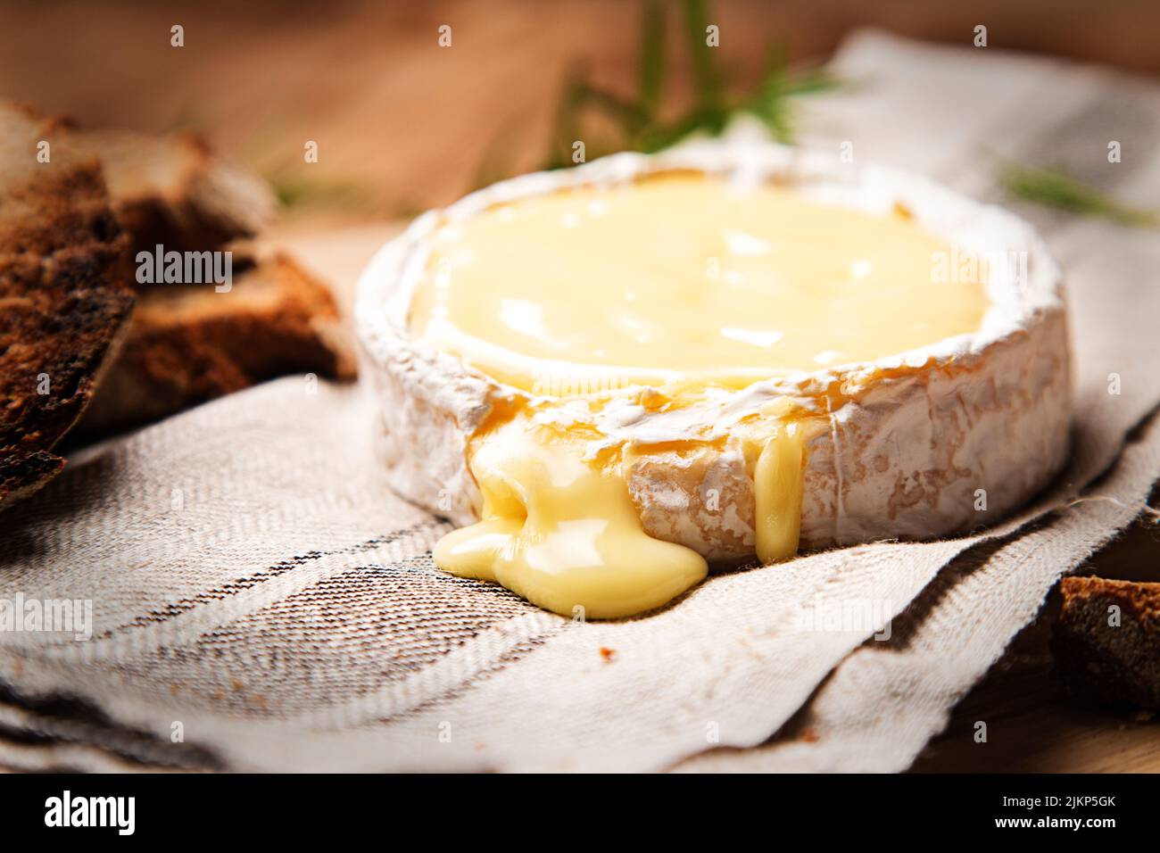 A closeup shot of baked camembert cheese on a cloth with sliced brown bread Stock Photo