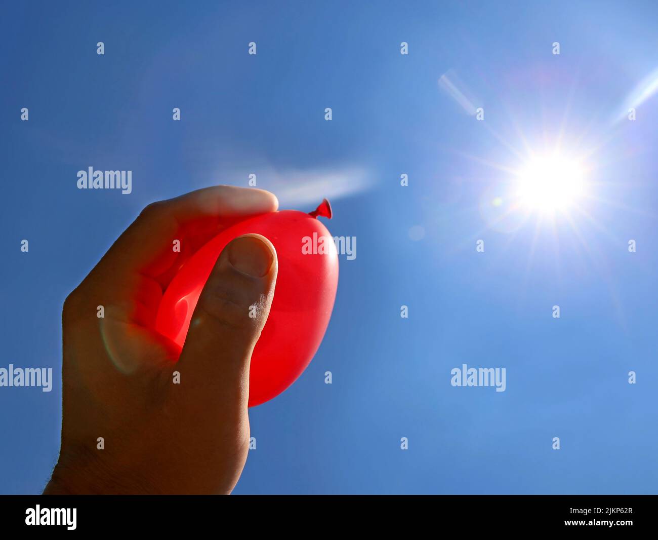 hand holds red water balloon against the summer sun, water bomb ready