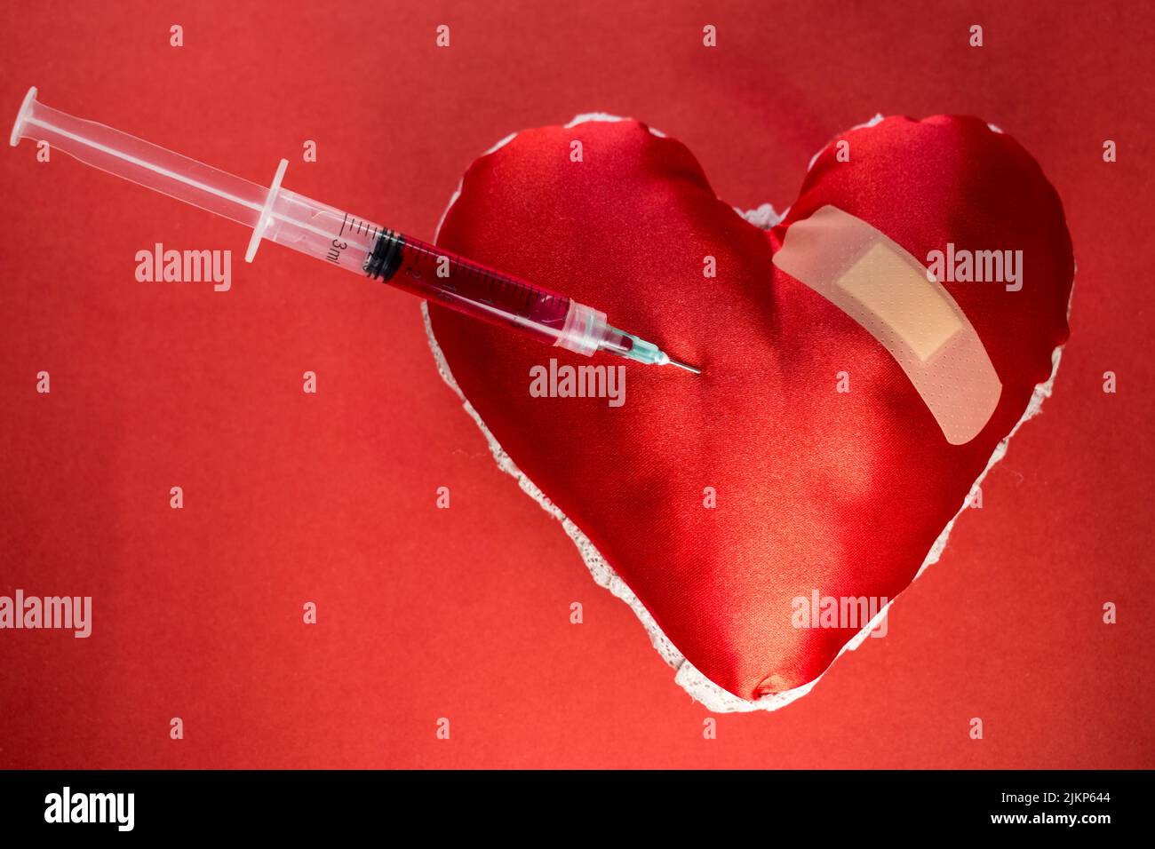 A background of blood donation theme with a syringe with blood in a heart shaped object Stock Photo