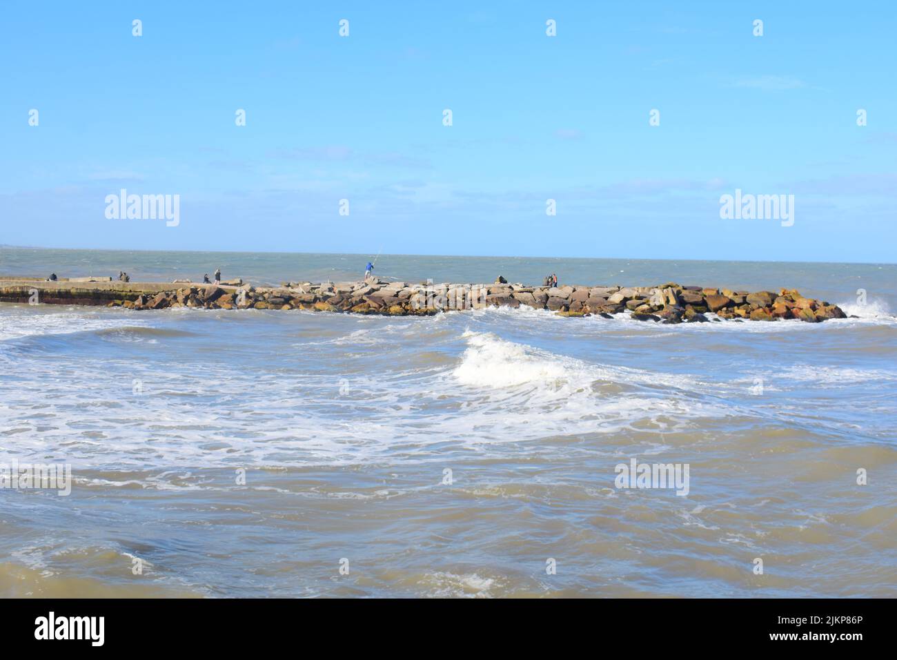 A Beautiful shot of a wavy sea crashing a sandy beach under a blue sky on a sunny day Stock Photo