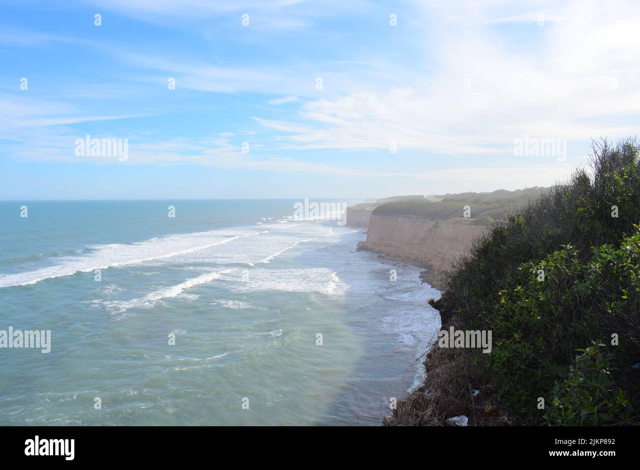 A beautiful shot of wavy sea crashing rocky cliffs under a blue sky on a sunny day Stock Photo
