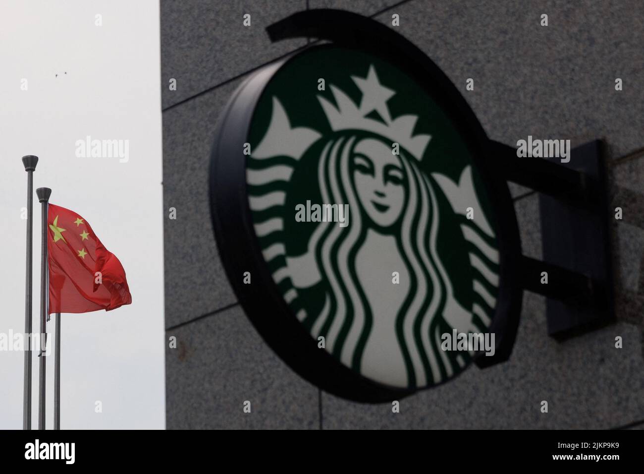 The Chinese flag flies near the Starbucks logo outside a cafe of the coffee chain in Beijing, China, August 3, 2022. REUTERS/Thomas Peter Stock Photo