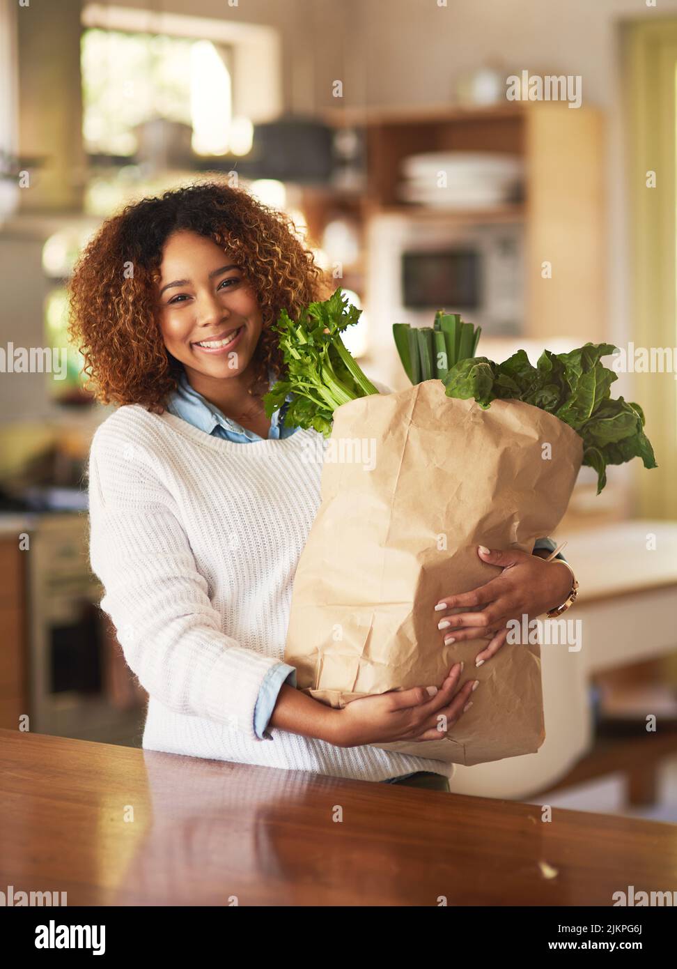 Healthy living begins at home. Portrait of a happy young woman holding a bag full of healthy vegetables at home. Stock Photo