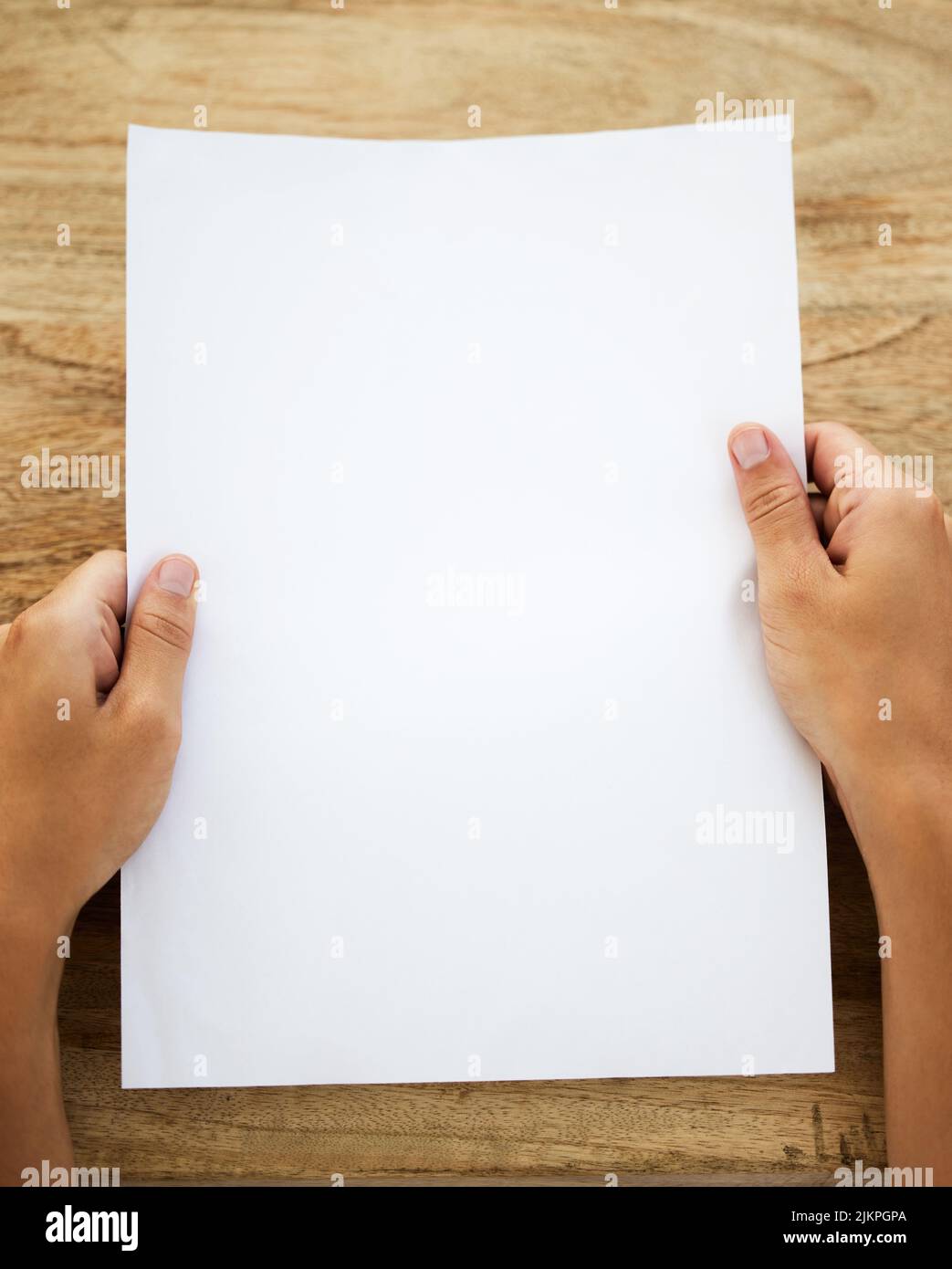 Let your creativity run wild. an unrecognisable person holding a blank piece of paper at a desk. Stock Photo