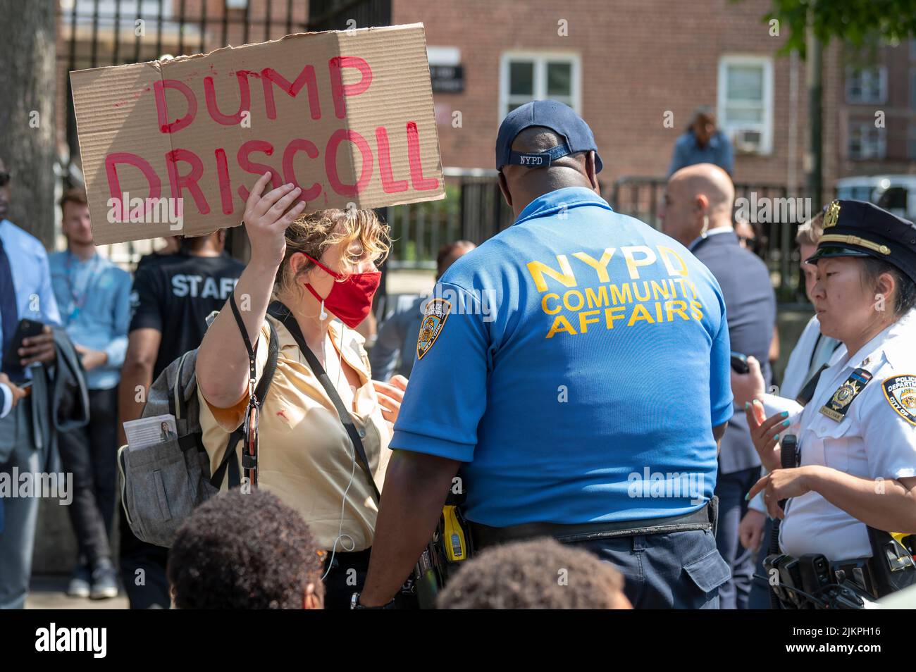 A woman peacefully holds a sign saying 'dump Driscoll,' urging Governor Hochul to replace NYPA interim president and CEO Justin Driscoll is surrounded by multiple NYPD officers at Woodside Houses NYCHA complex in Queens Borough of New York City. Governor Hochul and Mayor Adams announce $70 million initial investment to decarbonize NYCHA buildings as part of clean heat for all challenge. The plan calls for the installation of what's called an 'electric heat pump', developed by NYPA selected Midea America and Gradient, in 30,000 units, which would provide tenants in each apartment with the abili Stock Photo