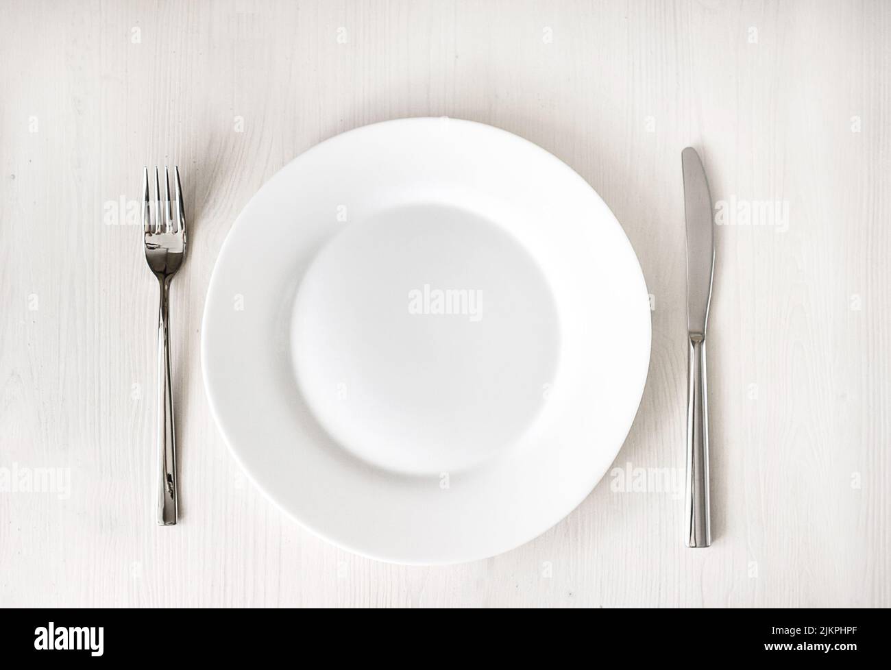White clean plate and stainless knife and fork on light wooden table. Served cutlery. Top view Stock Photo