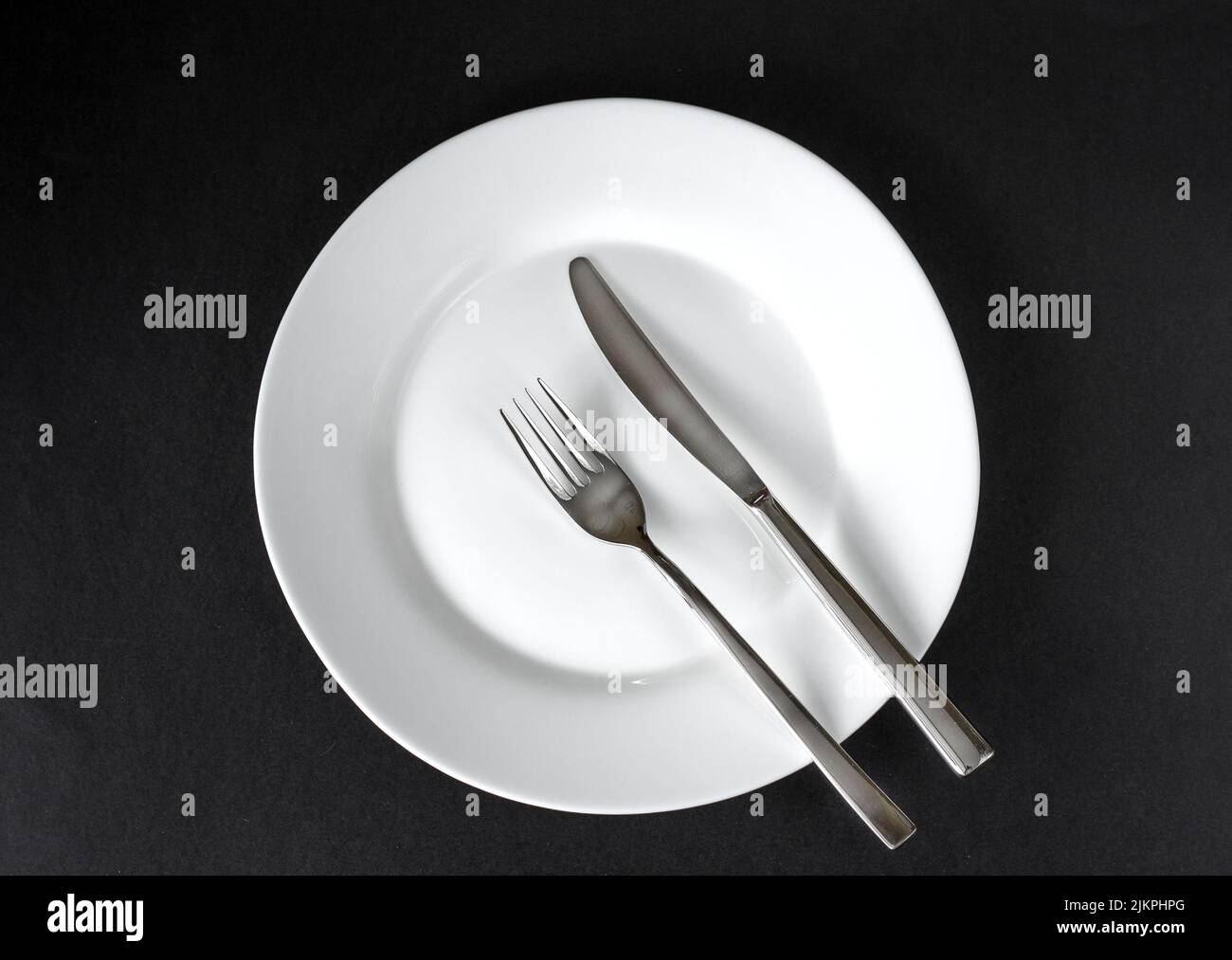 Served plate with cutlery. Empty white plate and stainless knife and fork isolated on black background. Top view. Studio shot Stock Photo