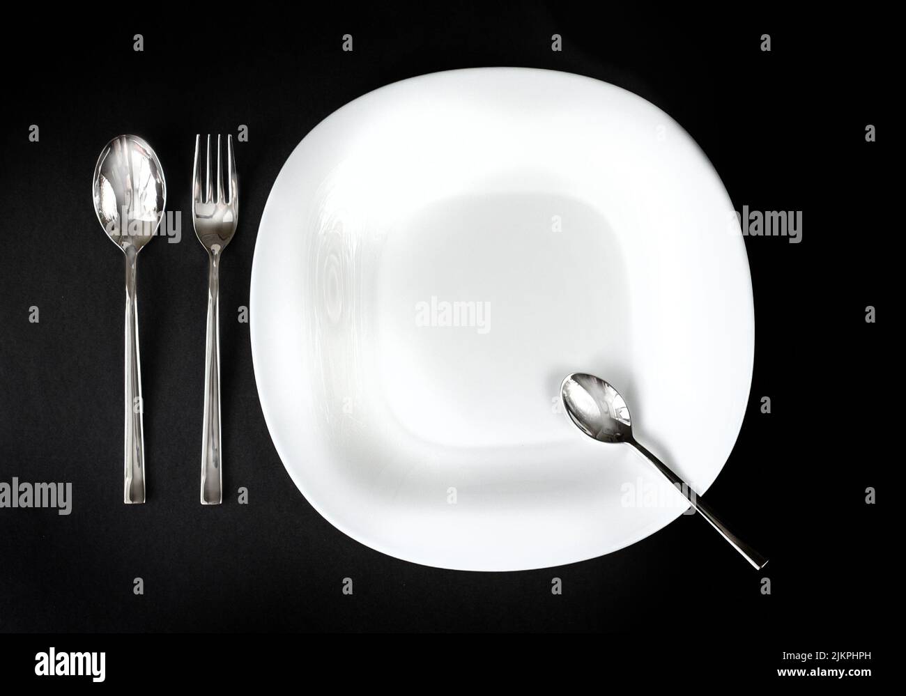 Served plate with cutlery. Empty white plate and stainless knife and fork isolated on black background. Top view. Studio shot Stock Photo