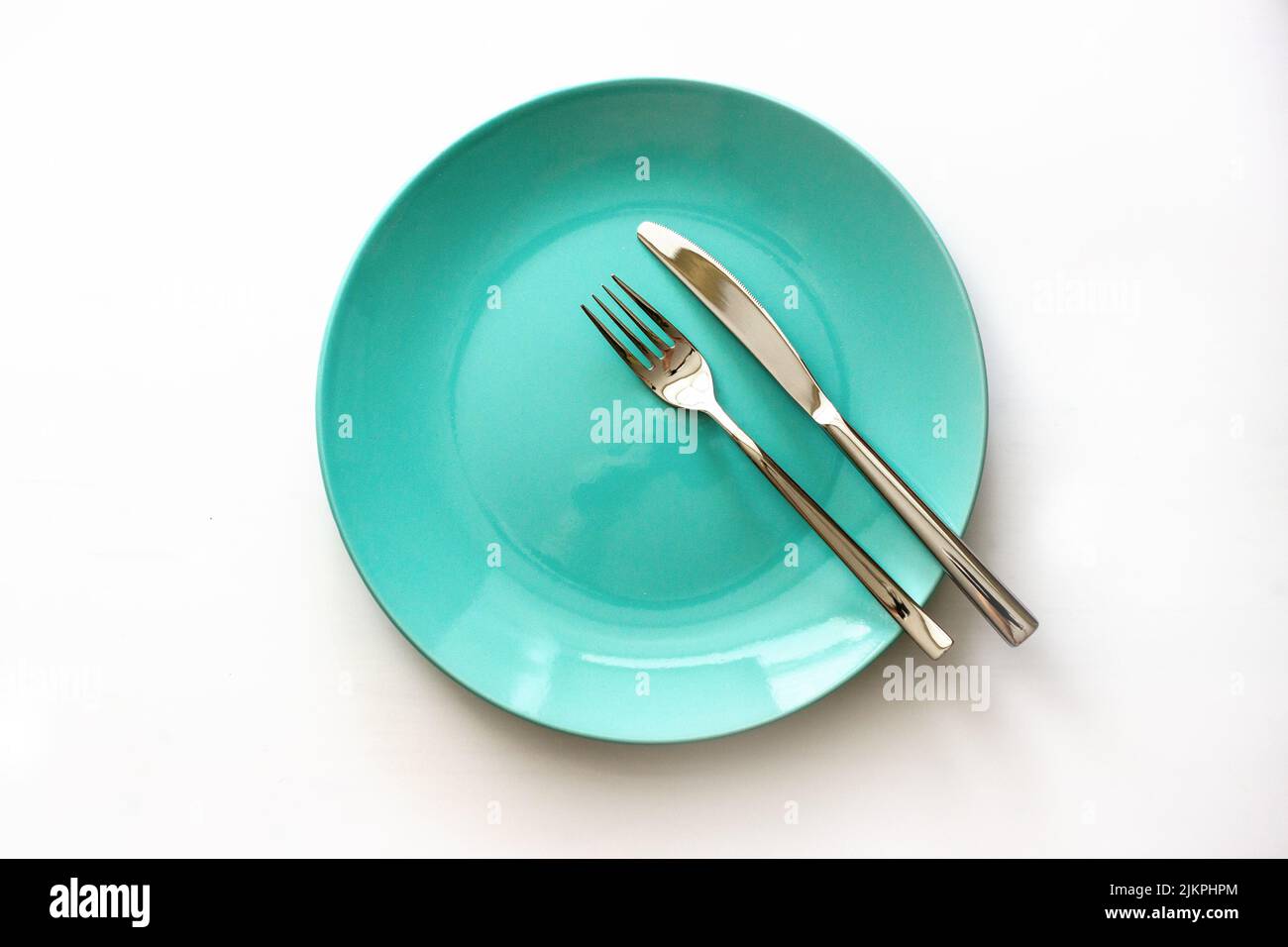 Served plate with cutlery. Empty green plate and stainless knife and fork isolated on white background. Top view. Stock Photo