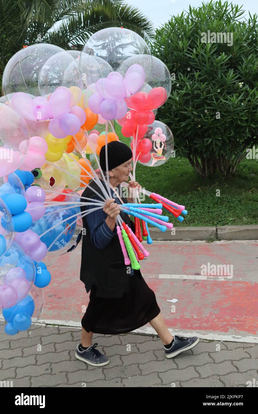 an old lady carrying balloons for sale walks along grimly Stock Photo