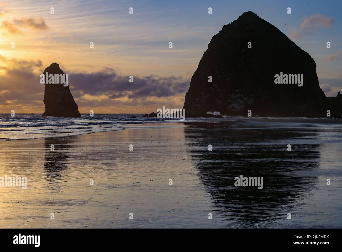 A silhouette of the Haystack Rock in Cannon Beach reflecting on the water surface at sunrise, Oregon, United States Stock Photo