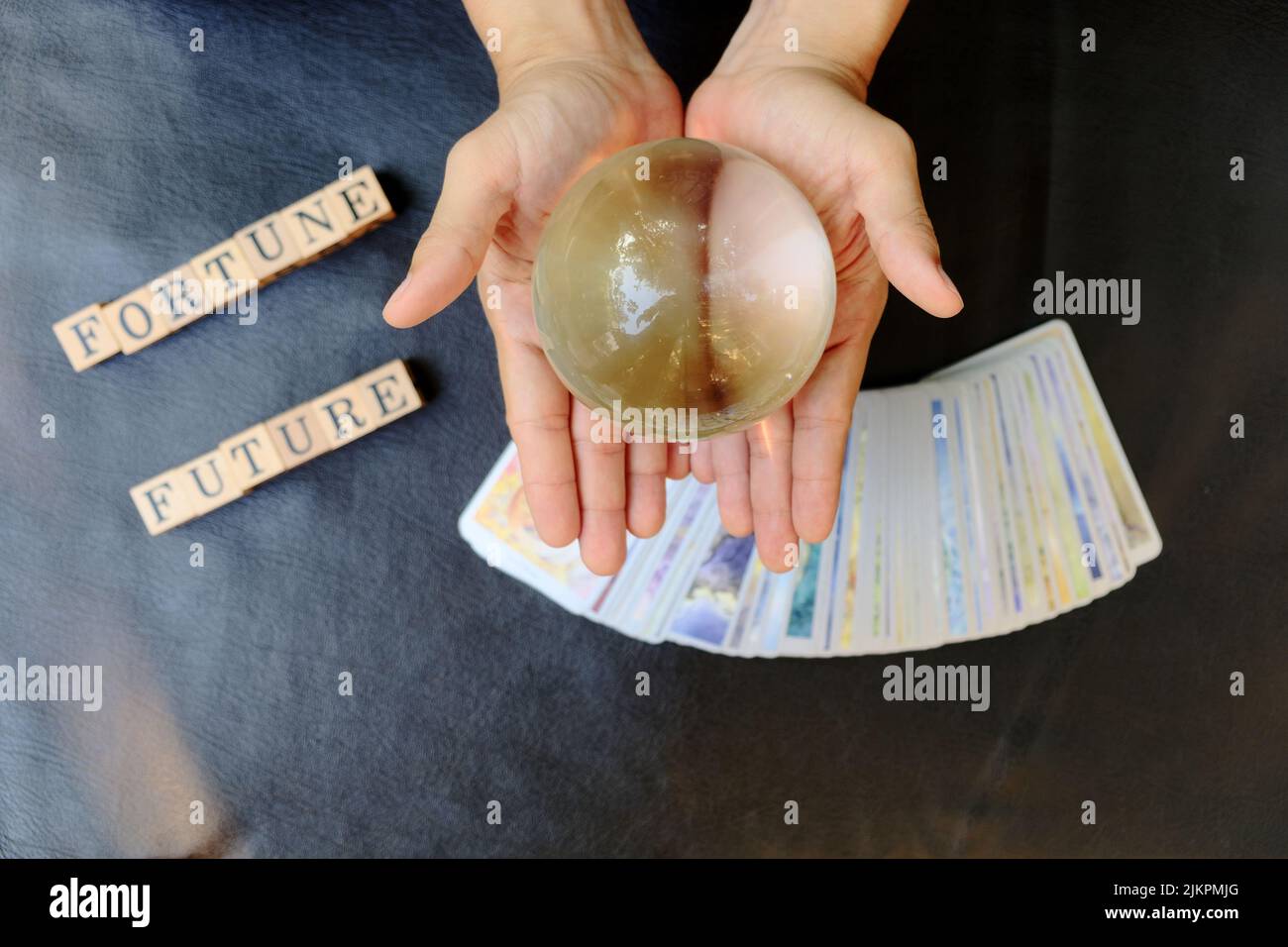 Close-up hands of fortune teller who show clear marble ball for prediction fate on tarot card and wood cube letter blurred background Stock Photo