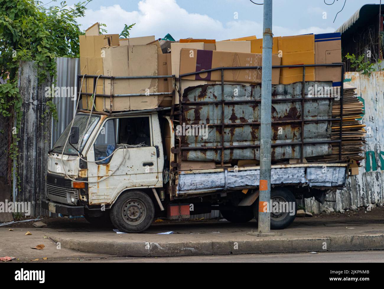 An old truck loaded with cardboard is parked on the sidewalk Stock Photo