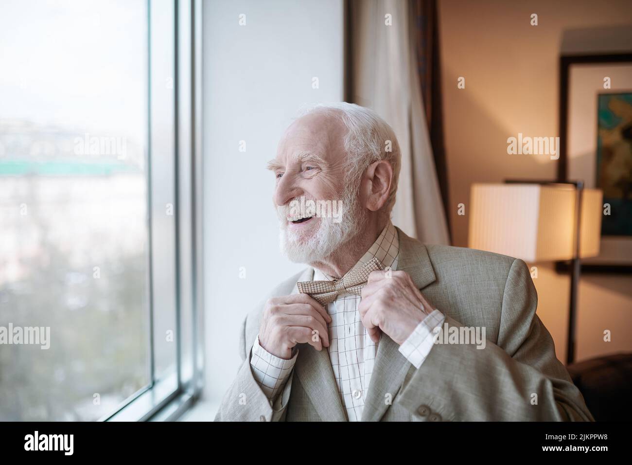 Smiling and happy elegant senior man standing near the window Stock Photo