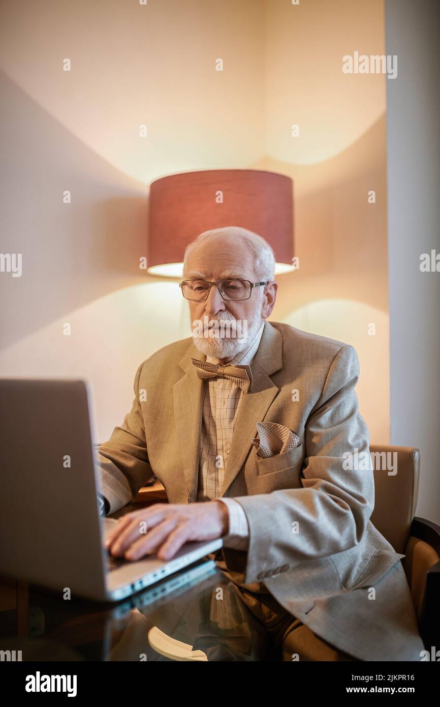 Senior man sitting at the laptop and looking busy Stock Photo