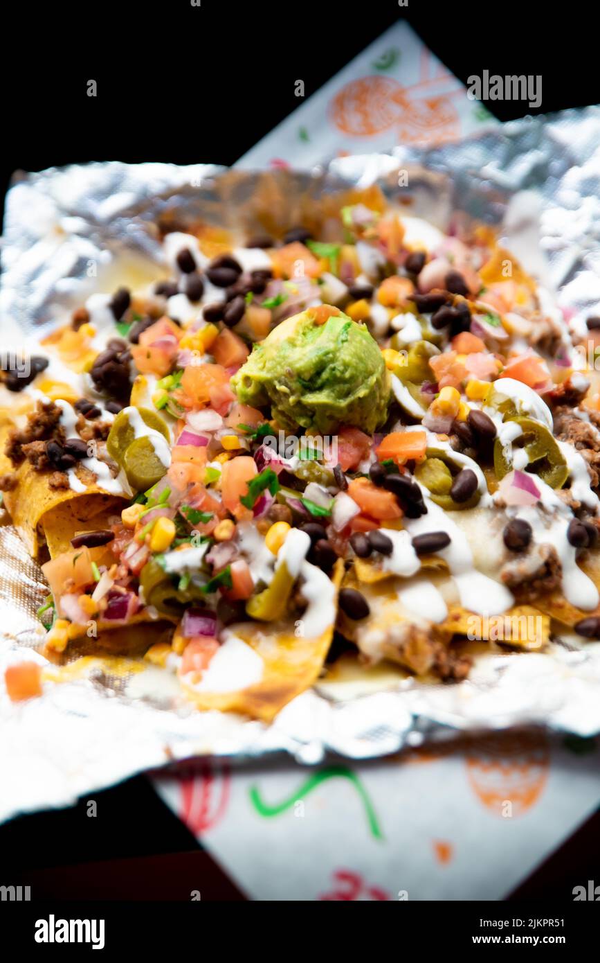 A vertical shot of Mexican nachos with sour cream, guacamole, and