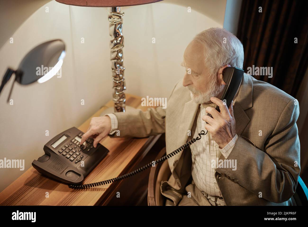 A gray-haired gentleman calling to the room service Stock Photo