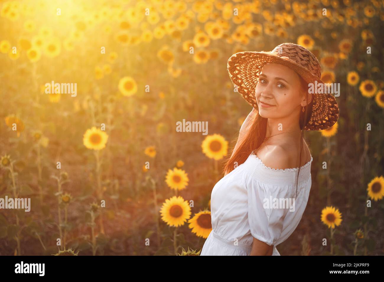 A young girl in a white dress and hat in a field of sunflowers at ...