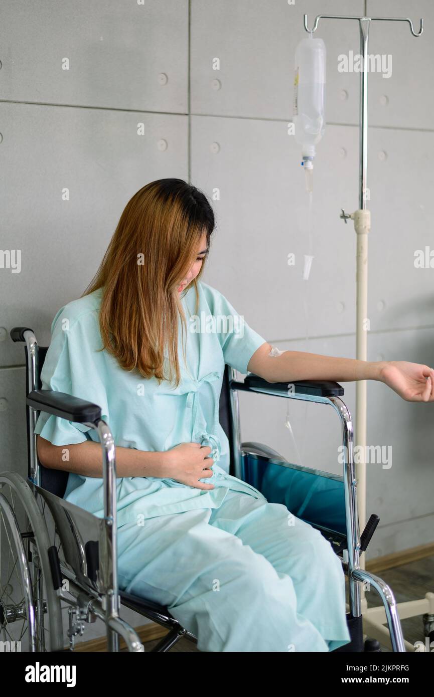 Woman patient on wheelchair having stomach ache waiting for check up in hospital Stock Photo
