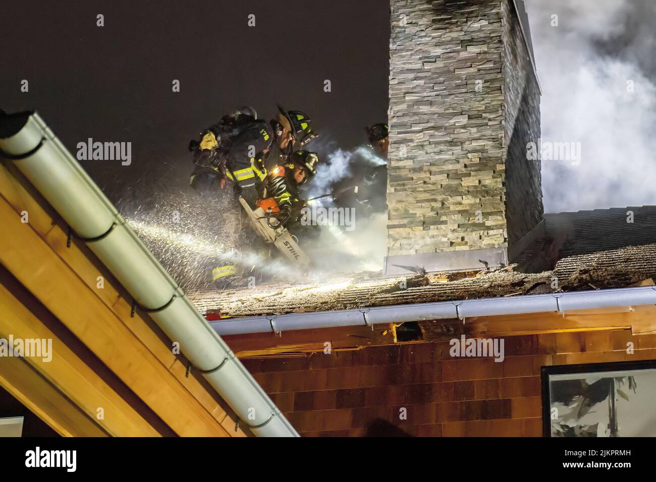 East Hampton firefighters use chain saws to cut holes in the roof ('ventilate') the roof as at 12:08 a.m. on Monday morning, 11/30/20, membrs of the E Stock Photo