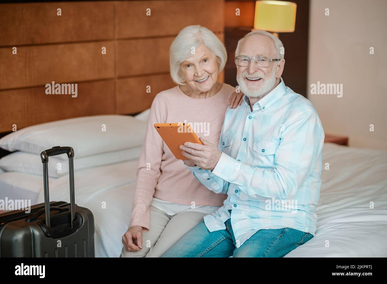 Senior couple sitting on a bed and watching something on a talet Stock Photo